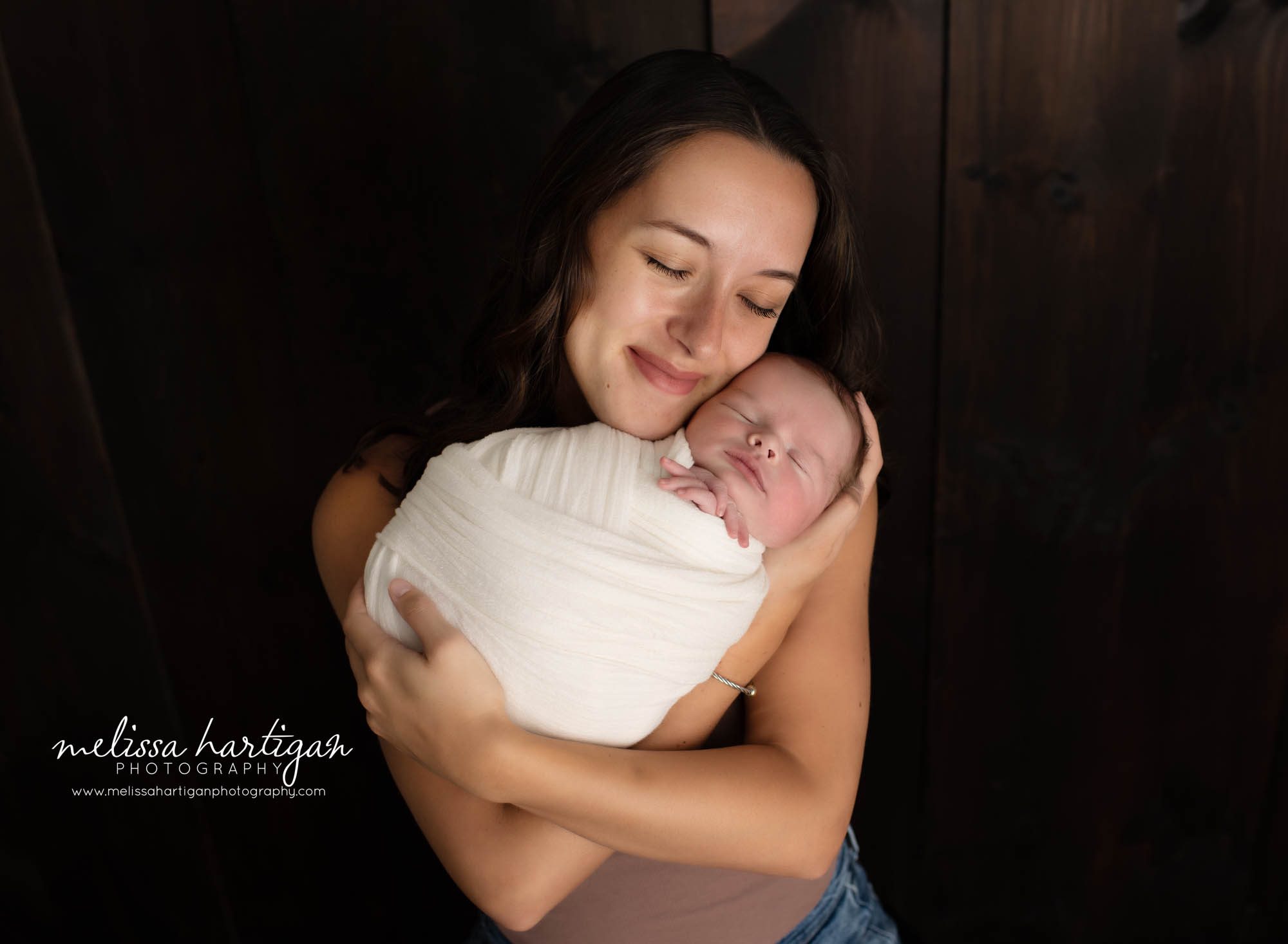 mom smiling holding newborn son wrapped in cream wrap in parents pose newborn photography photoshoot in connecticut