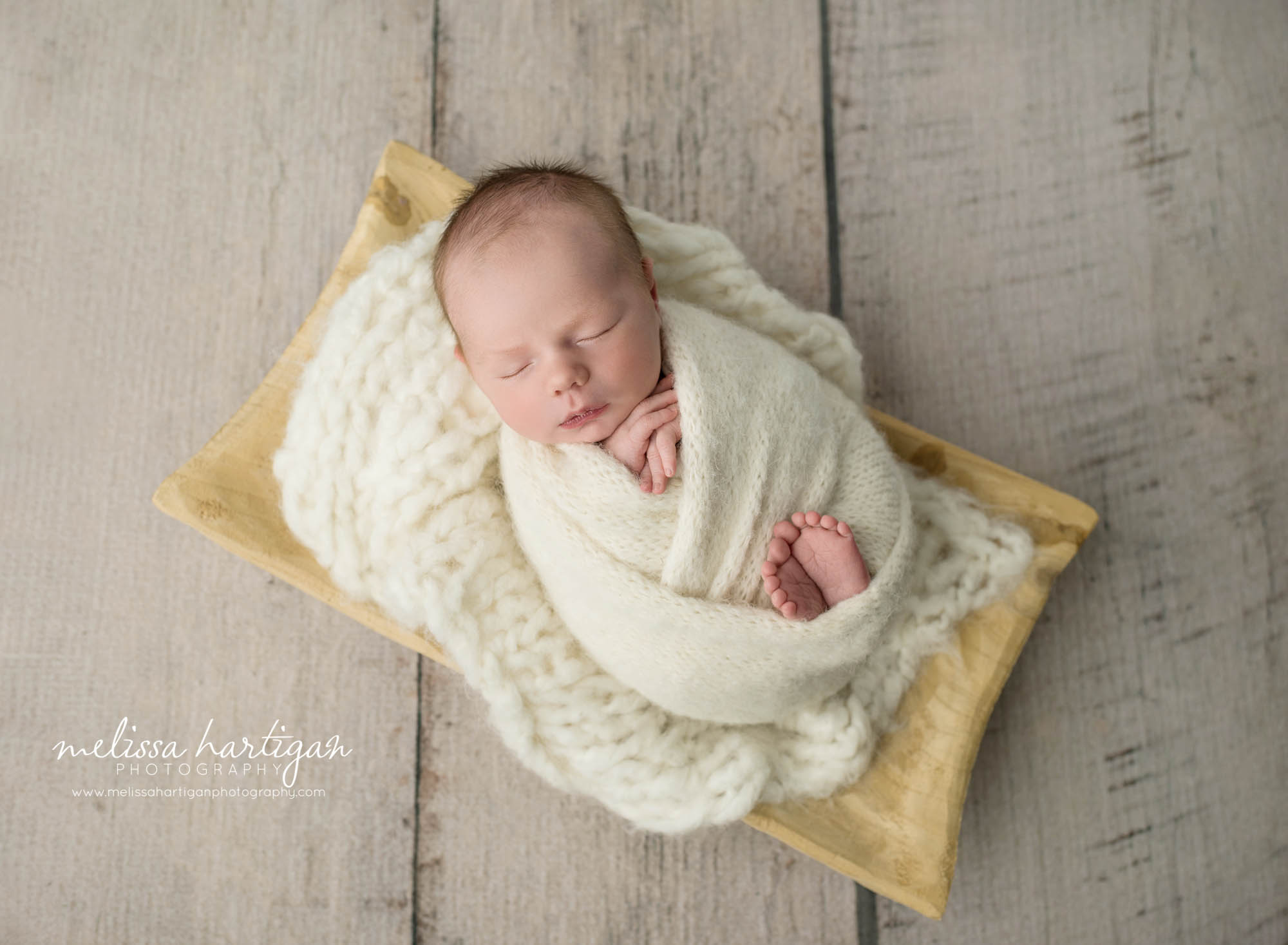 newborn baby boy wrapped in cream wrap posed in wooden bowl