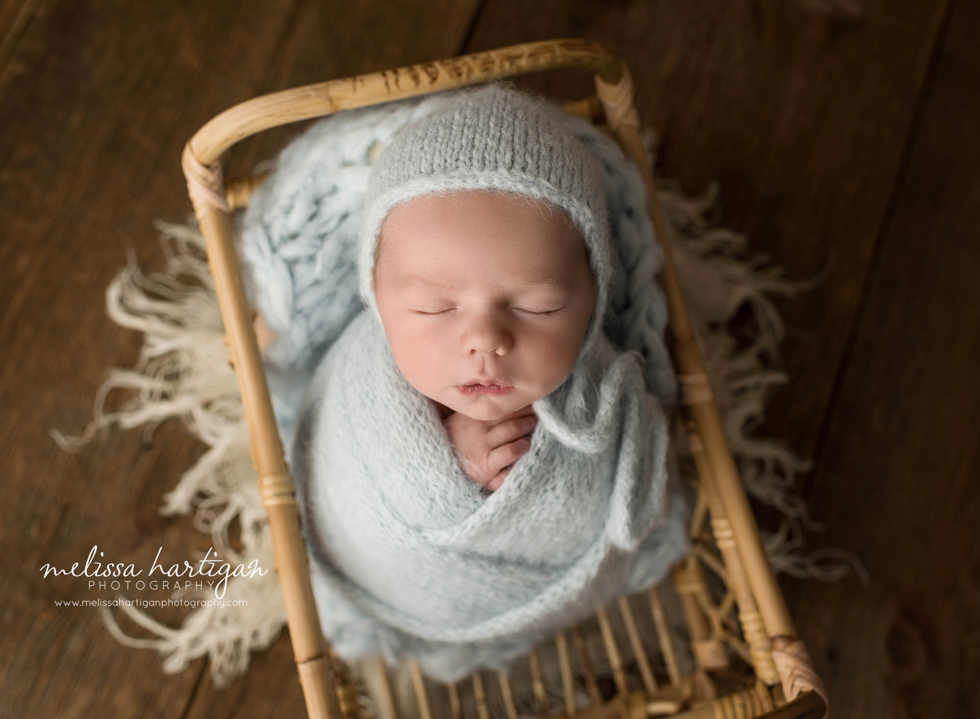 newborn baby boy wrapped in blue knitted wrap wearing light blue knitted bonnet fairfield county newborn photography