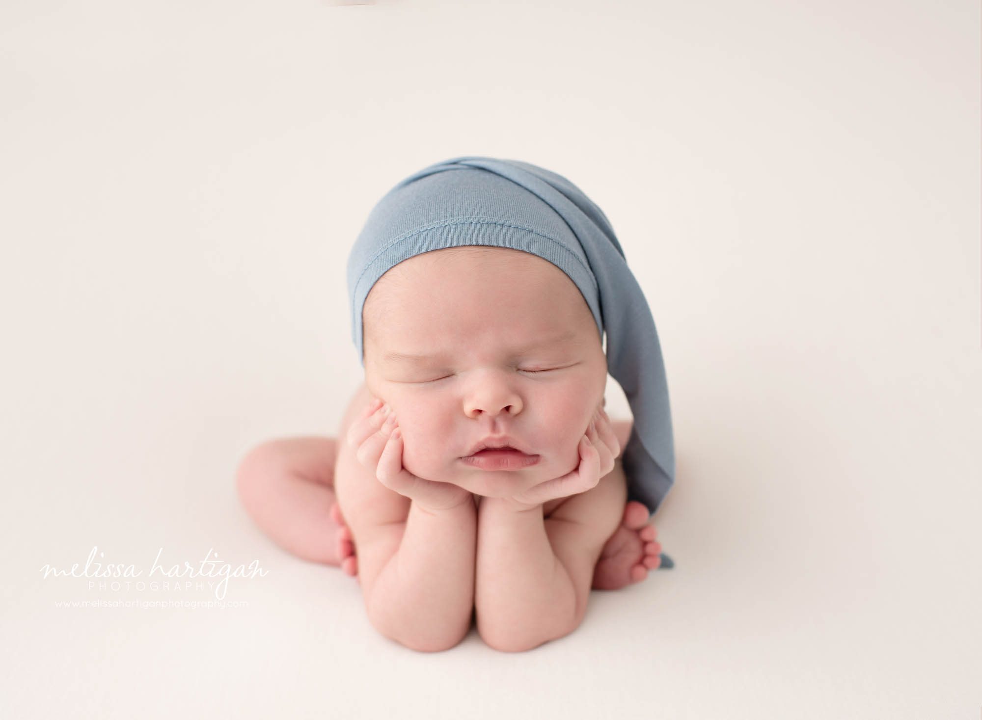 newborn baby boy posed froggy pose wearing blue sleepy cap