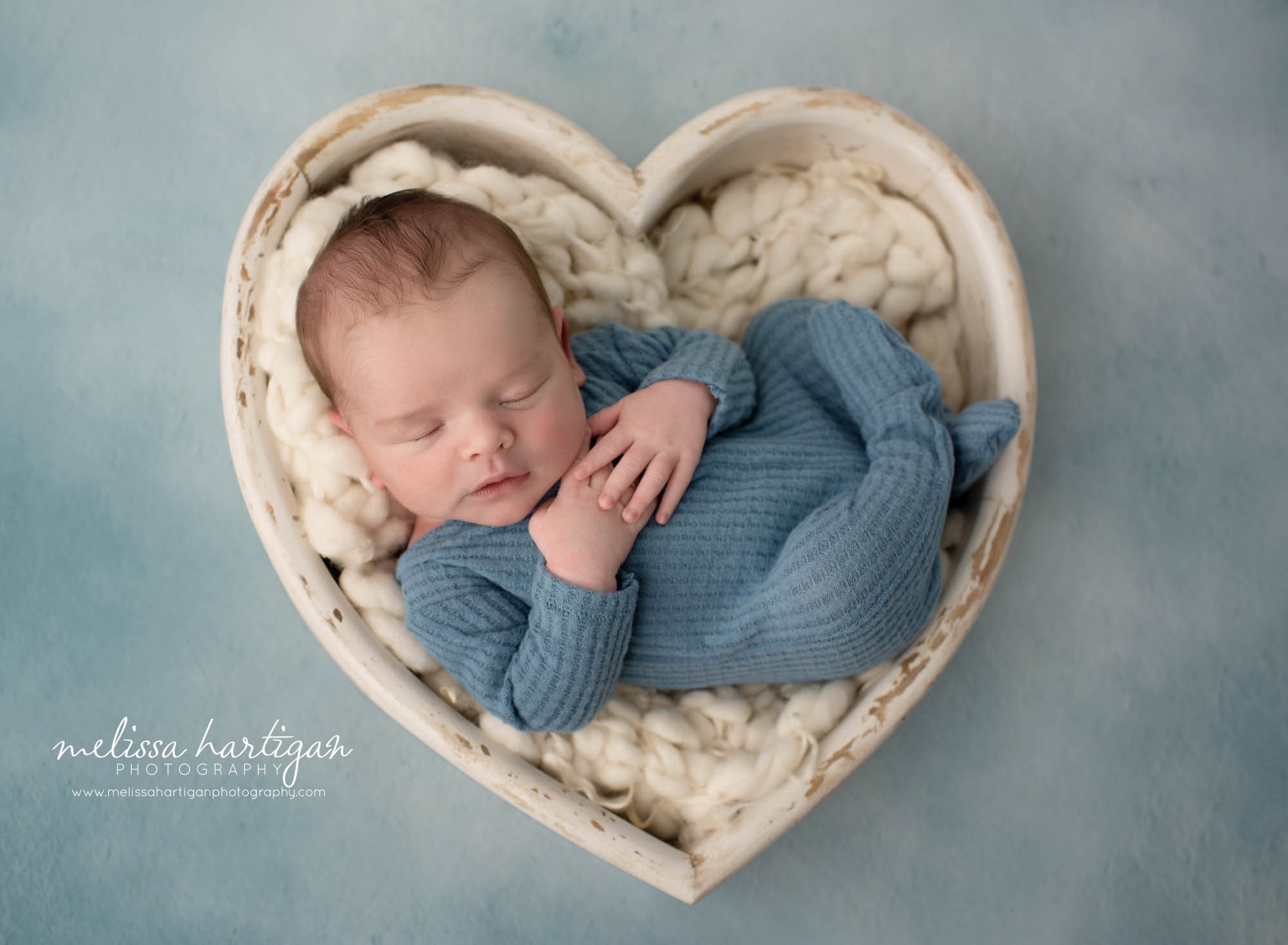 newborn baby boy wearing blue outfit posed in cream wooden heart bowl prop with cream fluff CT maternity newborn photographer