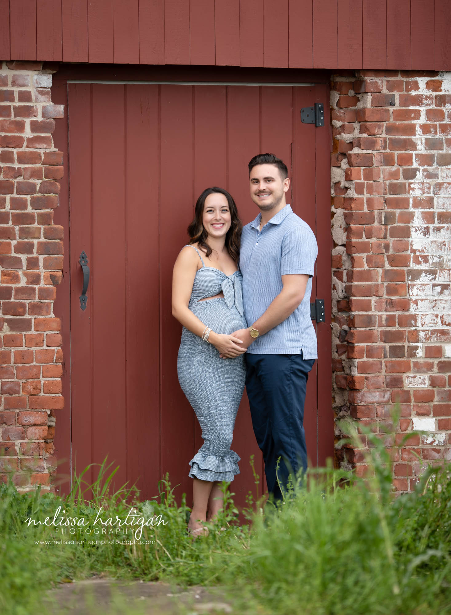 expectant couple standing next to red door on building maternity picture