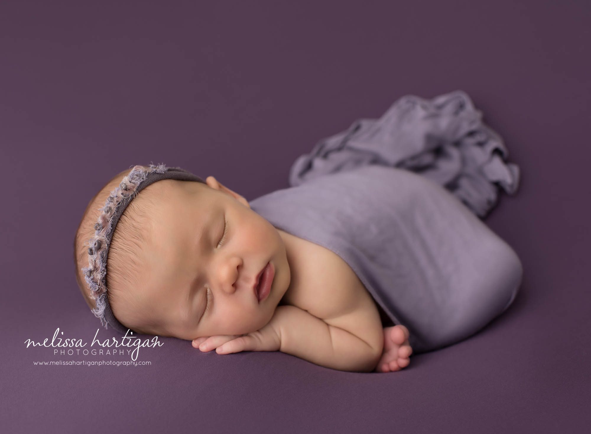 newborn baby girl posed on purple backdrop modified taco pose with purple wrap draped over newborn photography amston ct