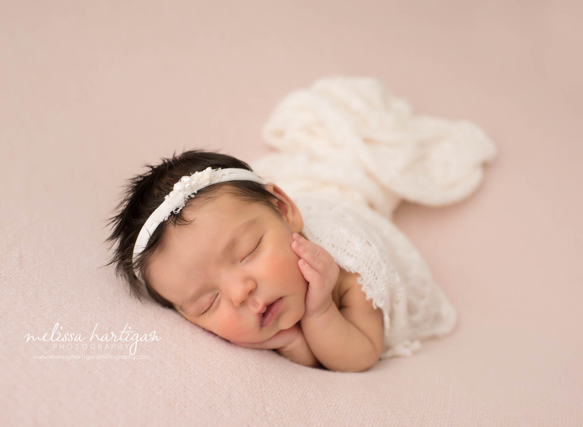 newborn baby girl posed on pink backdrop with cream layer draped over hear wearing headband newborn photography middletown