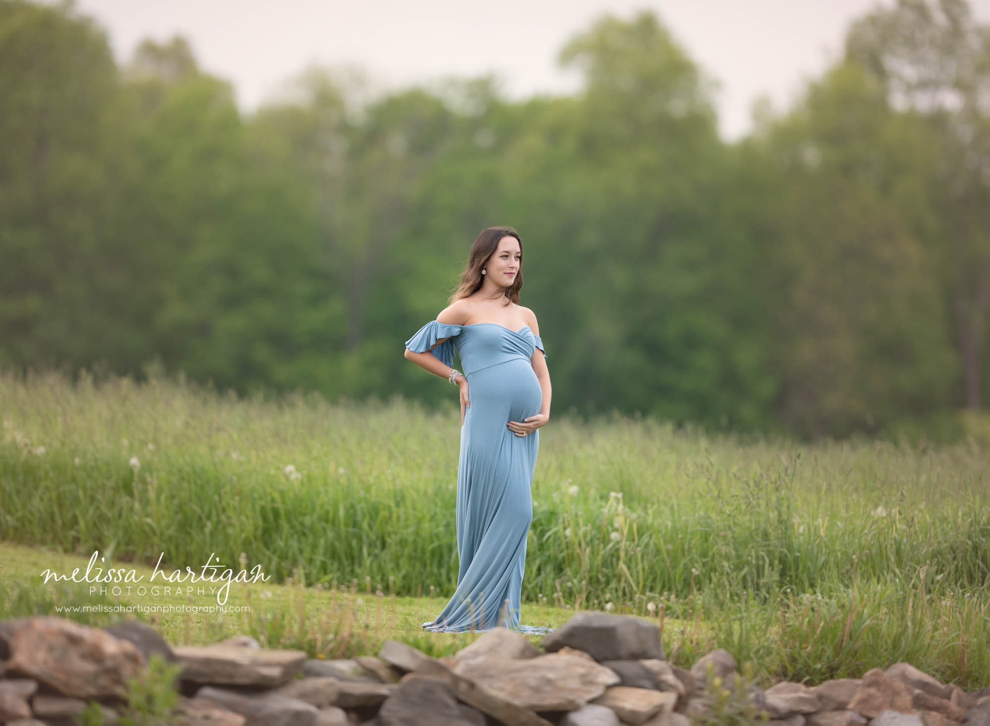 mam standing holding baby bump wearing blue long maternity dress