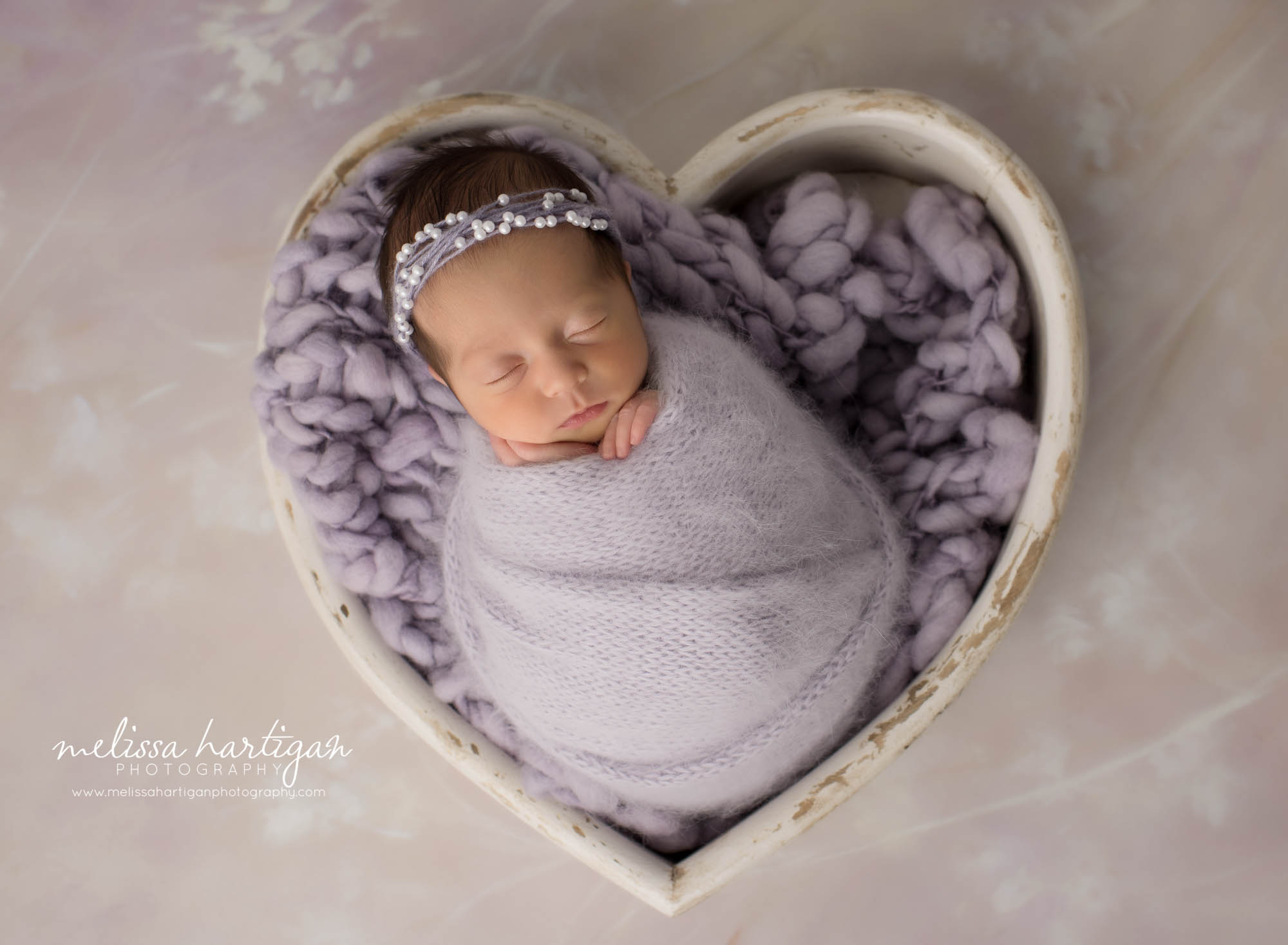 newborn baby girl wrapped in lavender purple wrap posed in wooden cream heart bowl prop wearing headband andover ct newborn photography