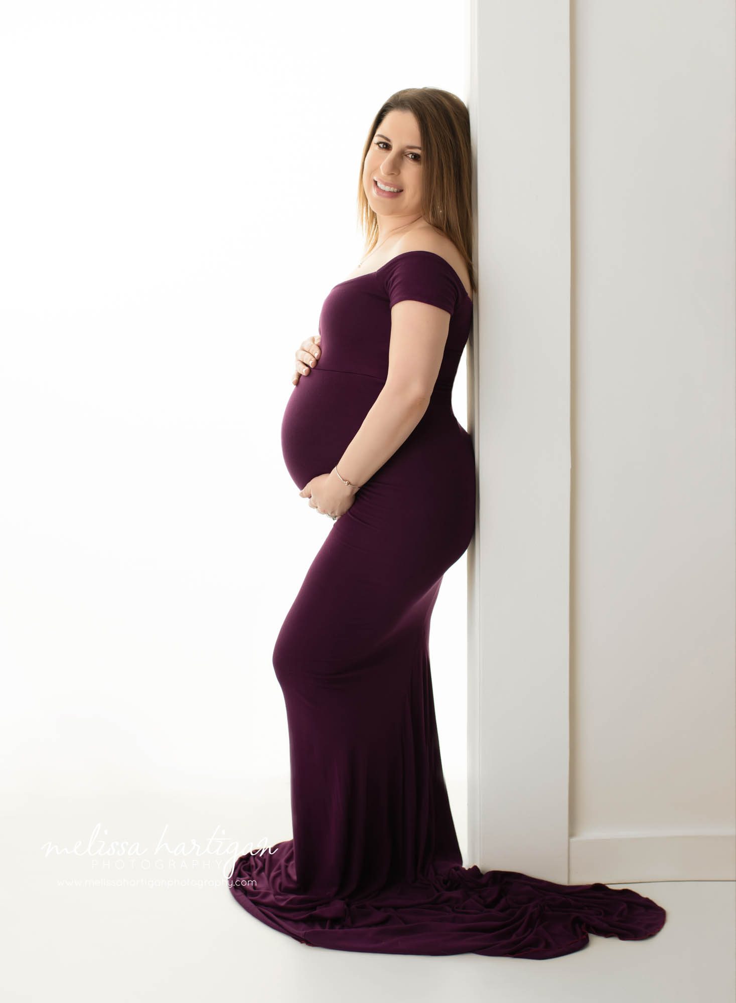 mom standing holding baby bump wearing long eggplant purple form fitting maternity gown CT maternity photography