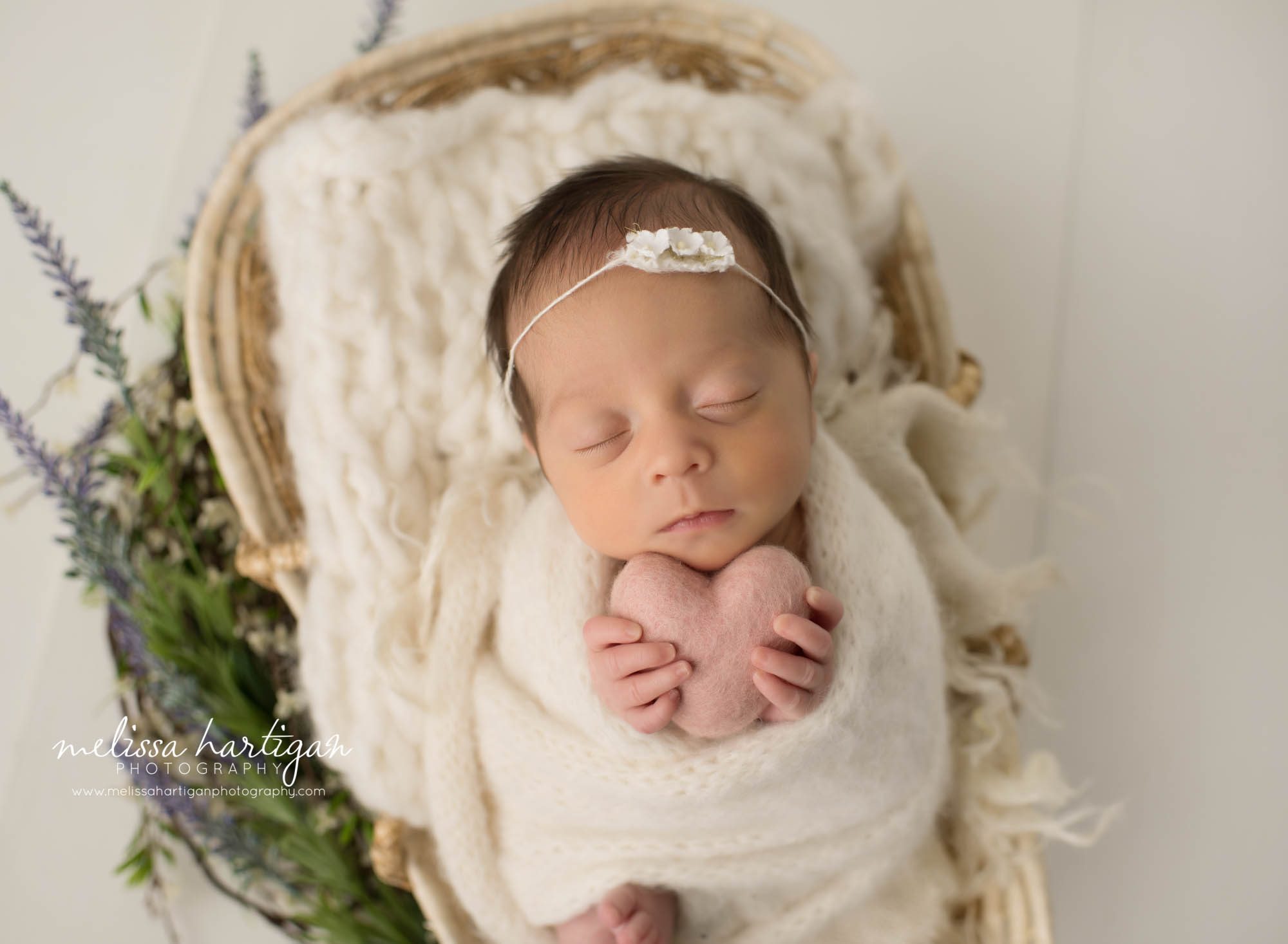 newborn baby girl wrapped wrapped holding felted heart posed in basket