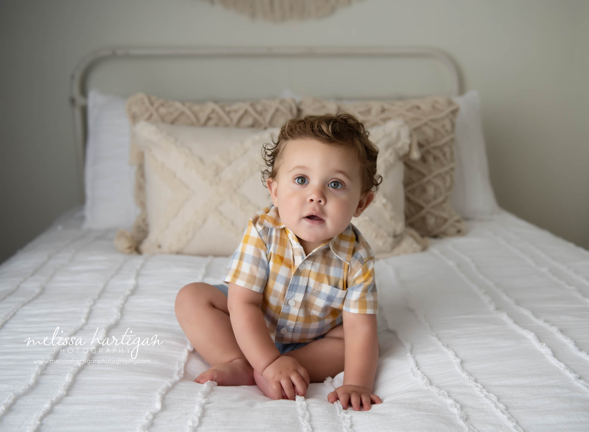 baby boy sitting on bed looking at camera curiously Connecticut baby photography