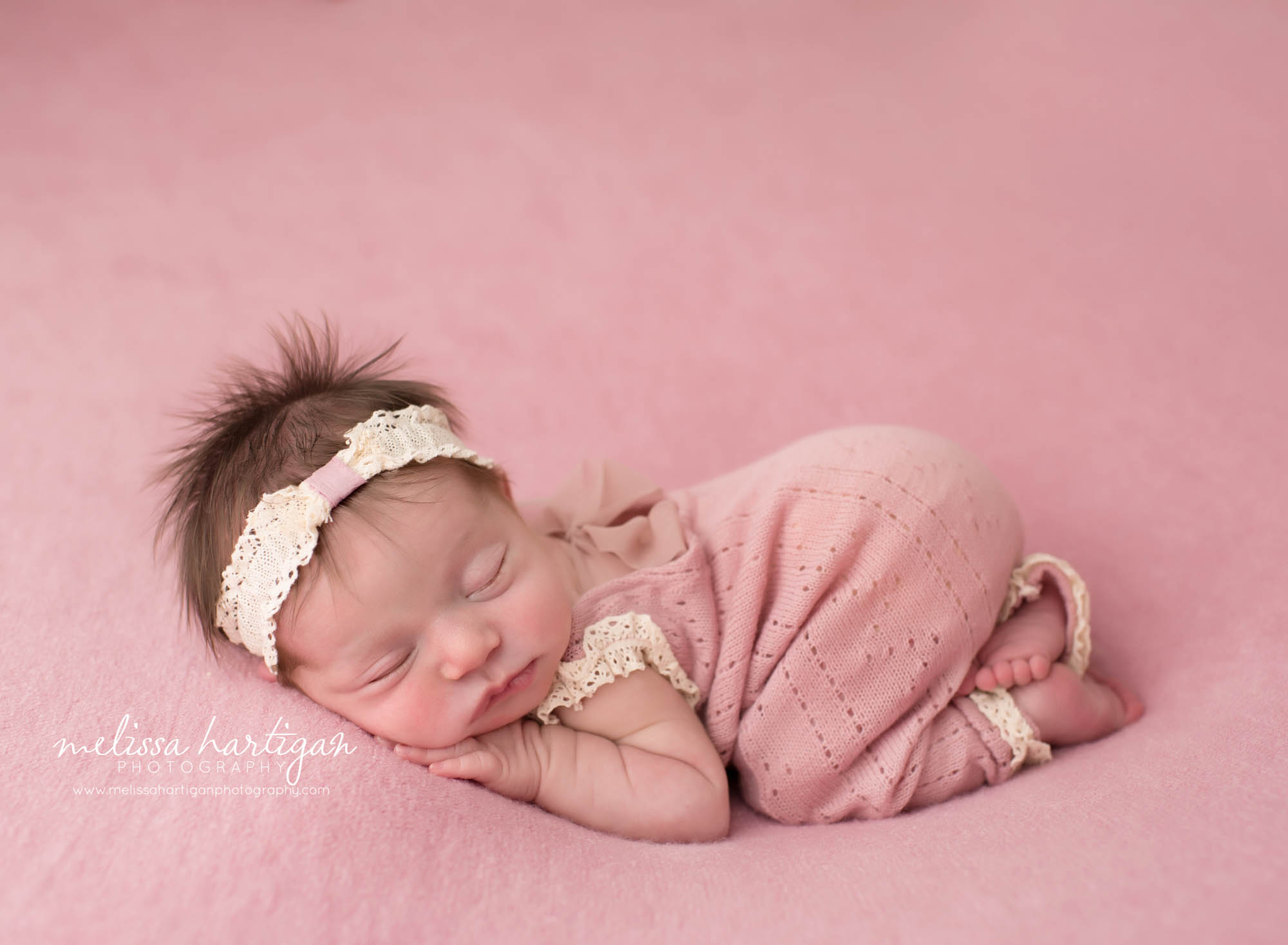 newborn baby girl posed bum up wearing pink newborn girl outfit and pink and cream lace headband