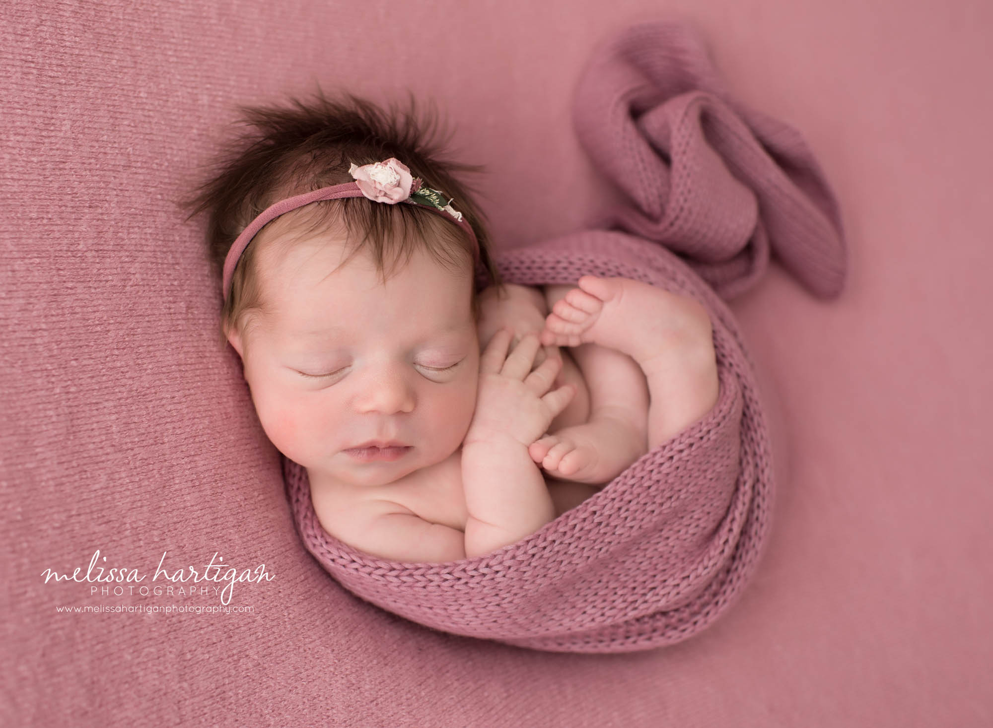 newborn baby girl posed in womb pose on pink backdrop
