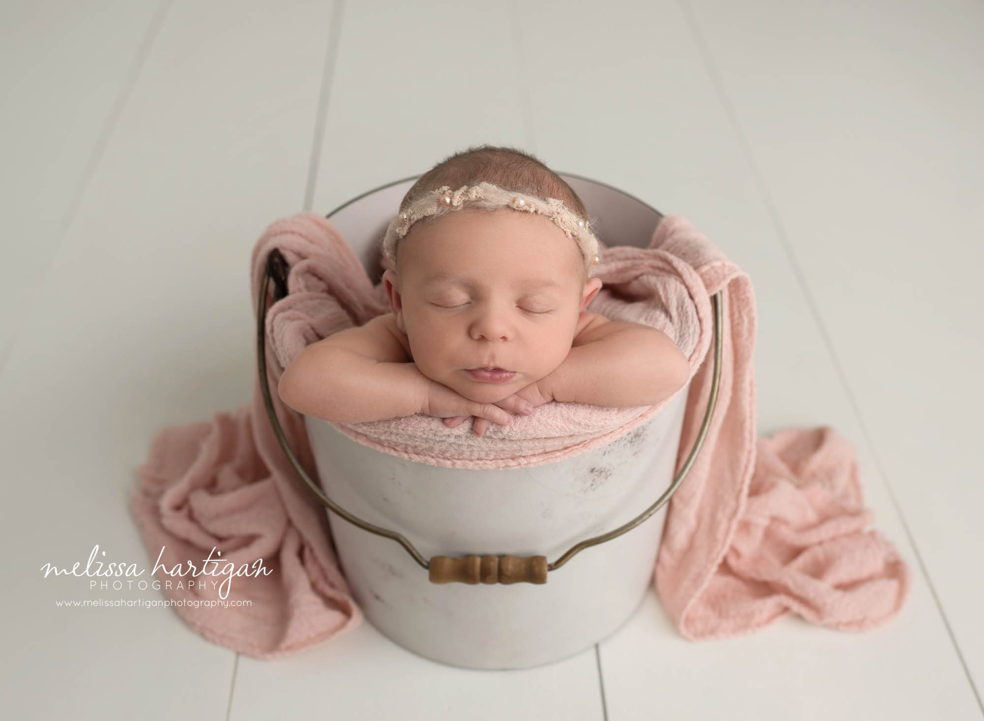 newborn baby girl posed in bucket with pink layer wrap