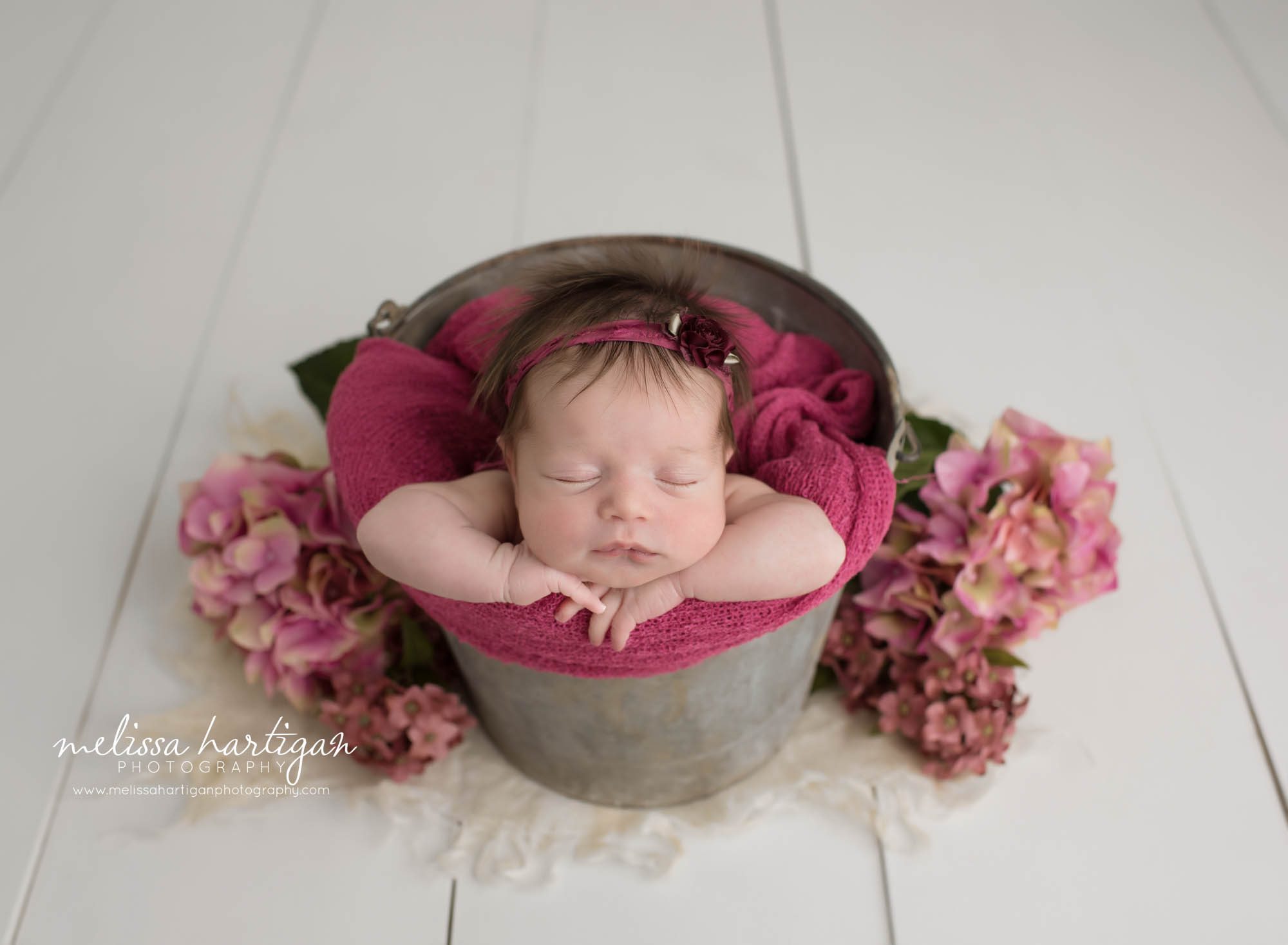 newborn baby girl posed on metal bucket with pink flowers wearing pink headband