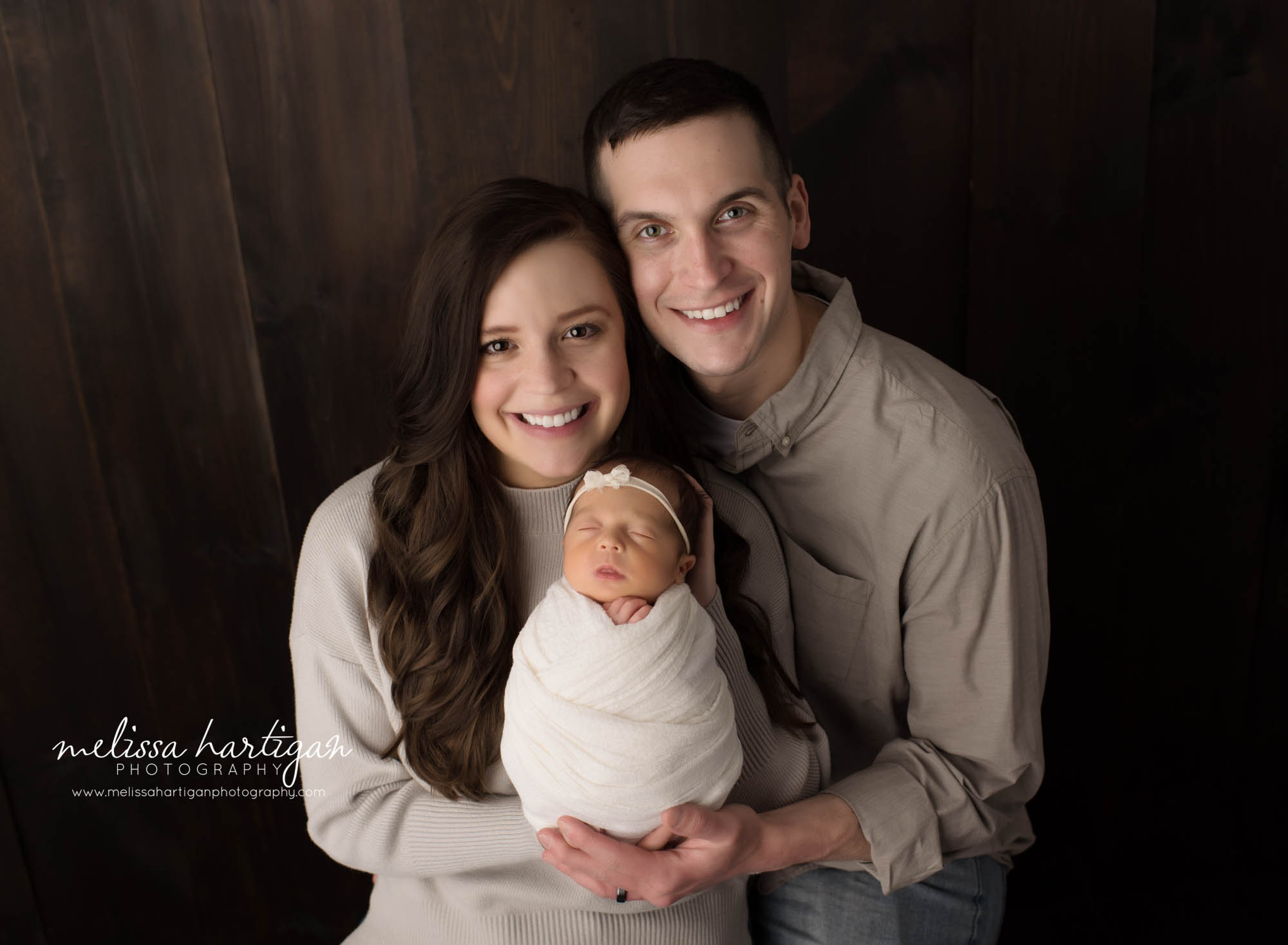 mom dad holding newborn daughter wrapped in knitted wrap family pose