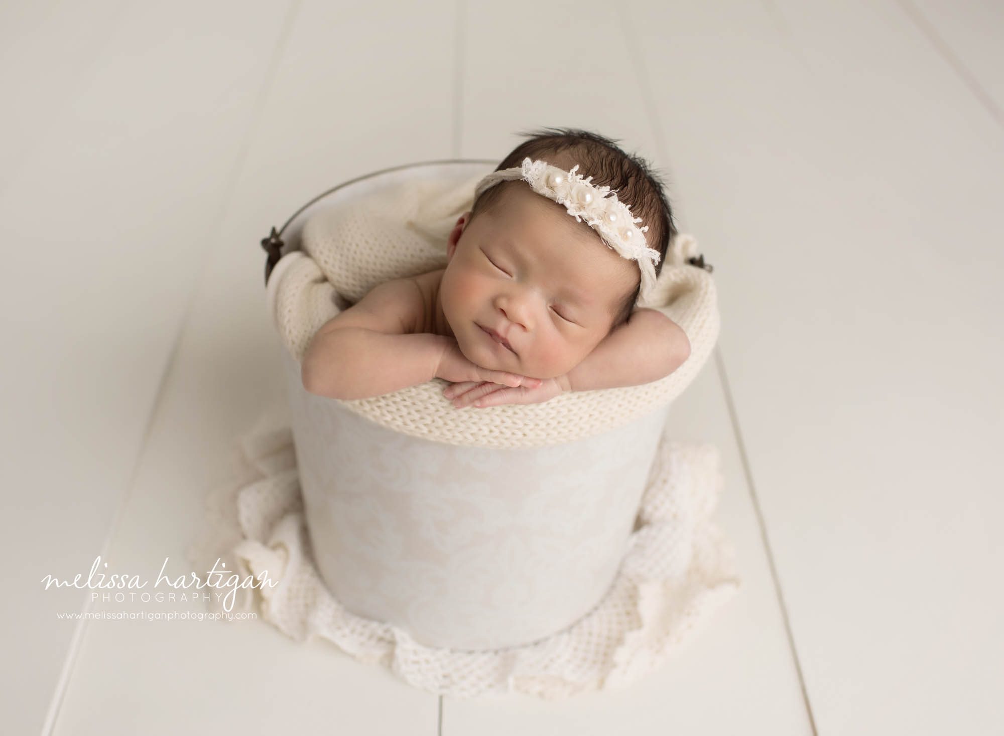 newborn baby girl posed in bucket with all white layers and flower headband hartford county newborn photography