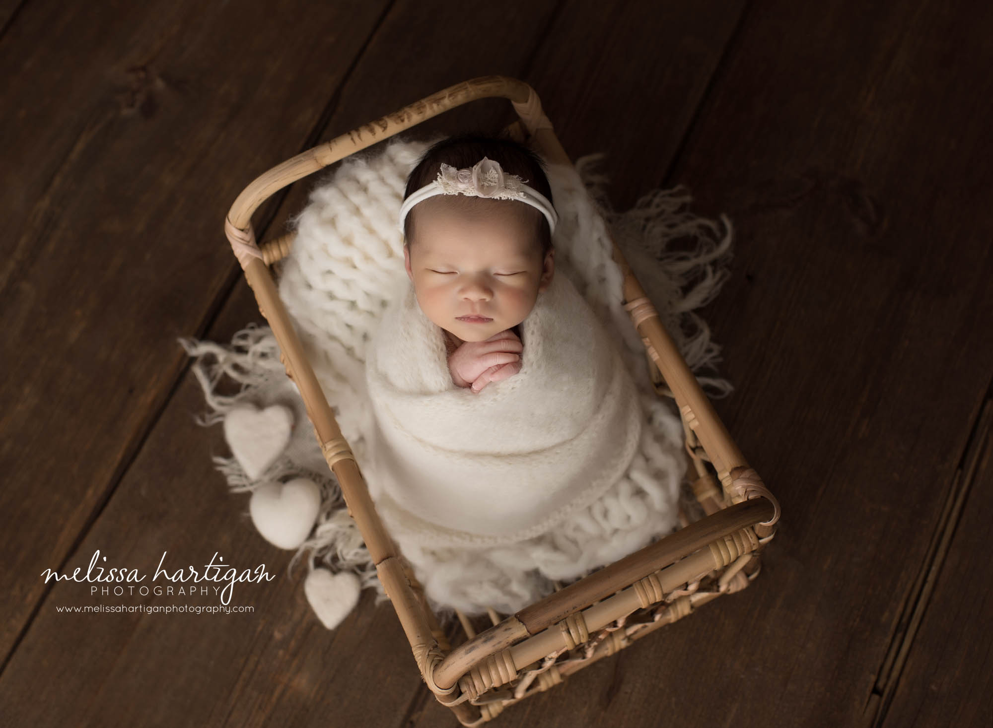 newborn baby girl wrapped in white knitted wrap posed in basket with white felted hearts newborn photoshoot