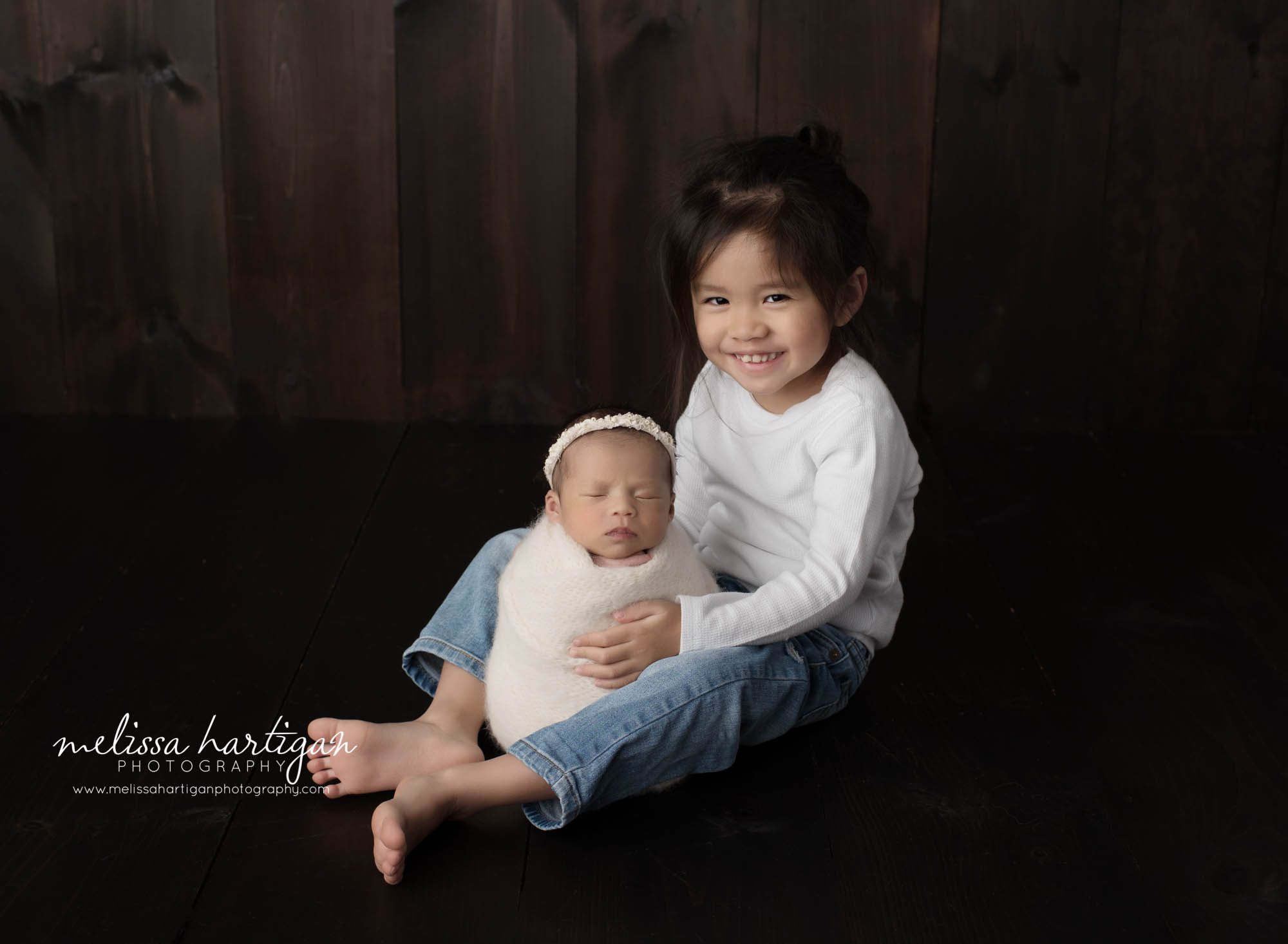 big brother sitting with newborn baby sister wrapped in white wrap sibling pose