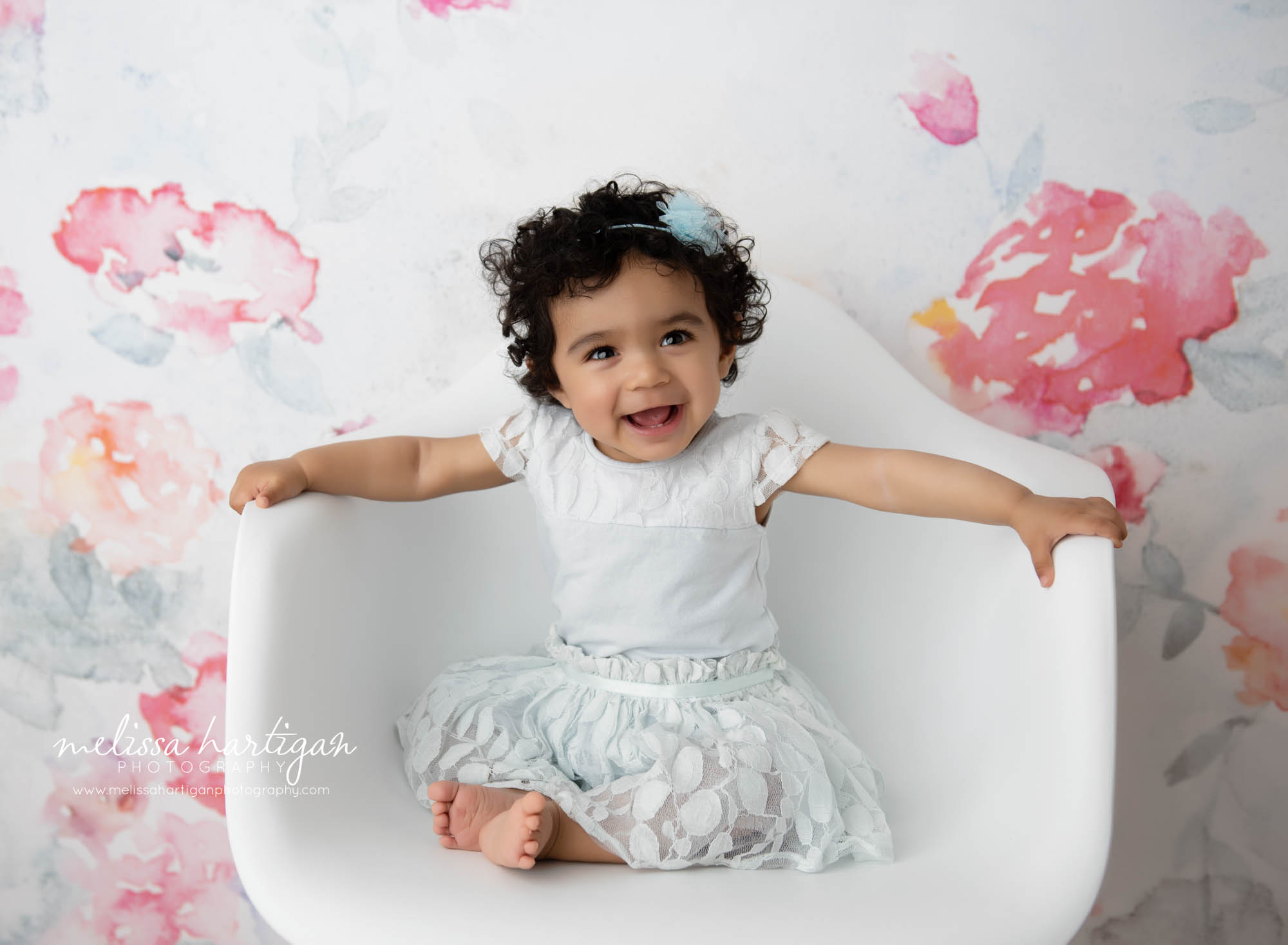 happy baby girl smiling laughing sitting on white chair in baby milestone photography studio