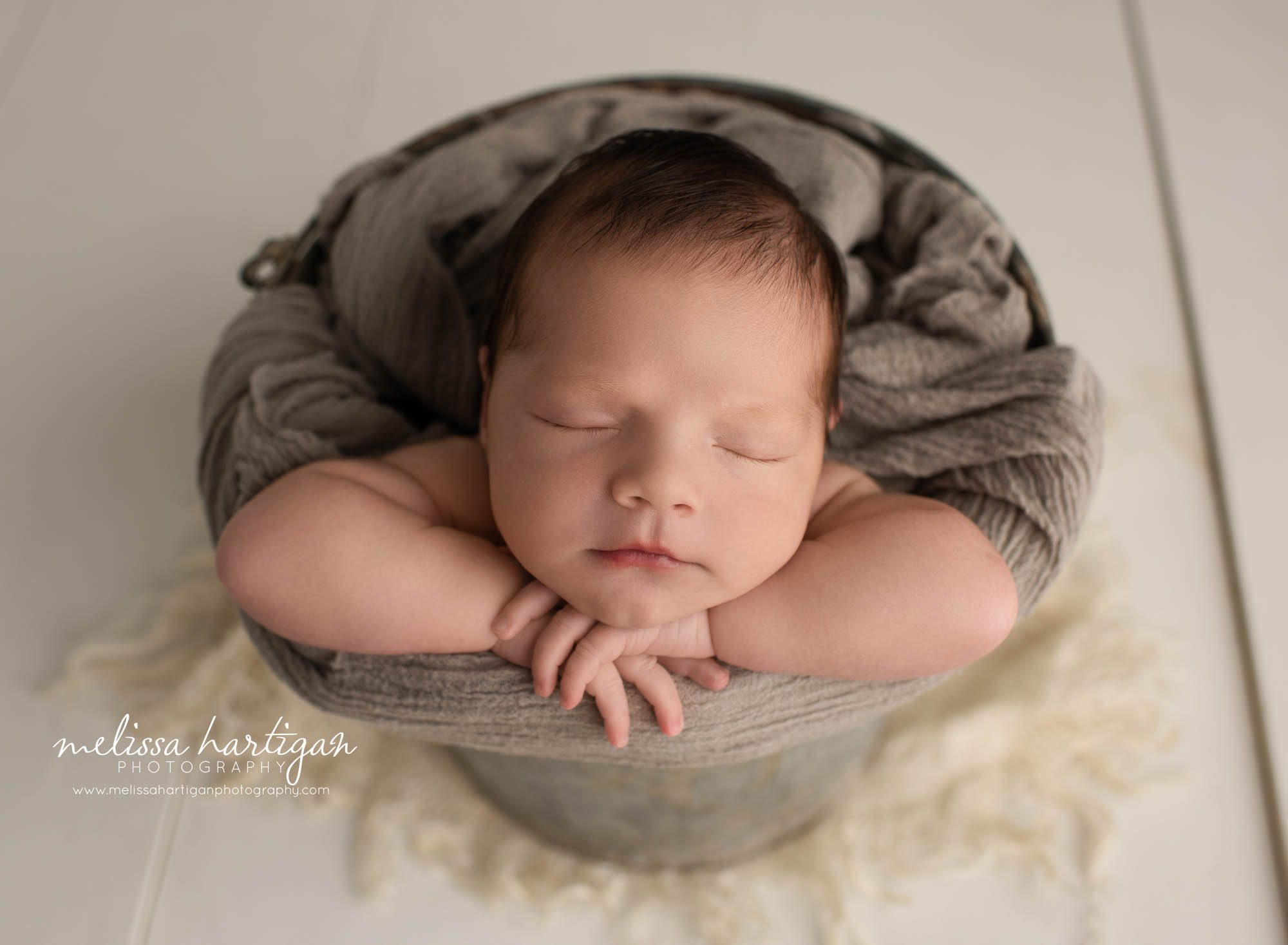 newborn baby boy posed in bucket with gray draping wrap