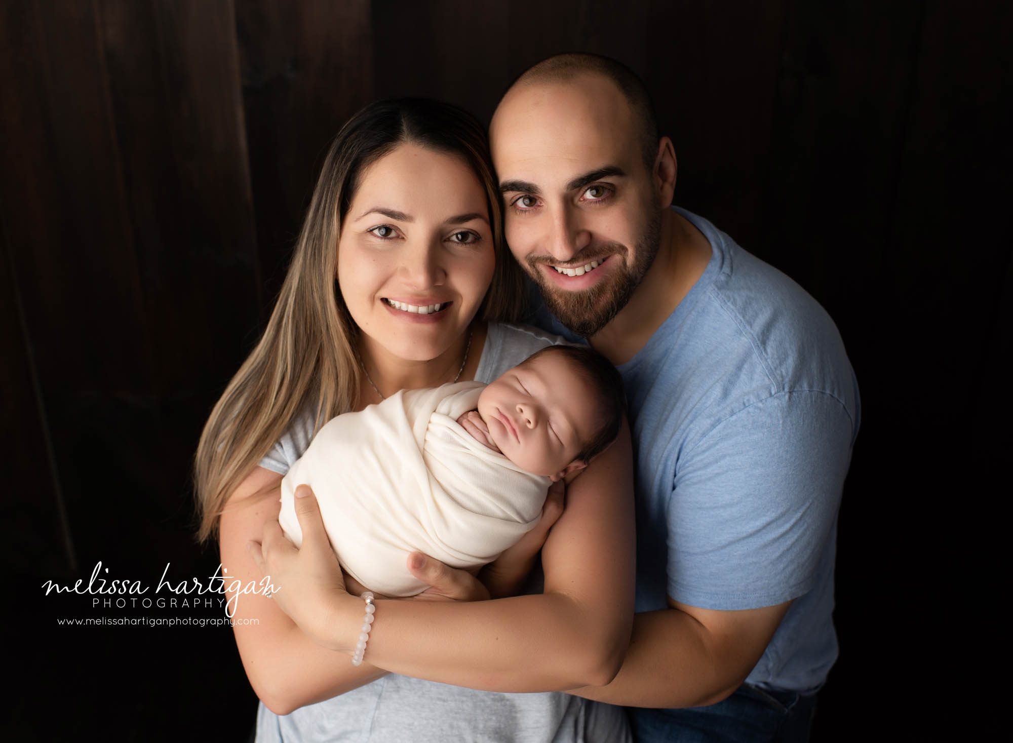 mom dad holding newborn son wrapped in white wrap for family pose