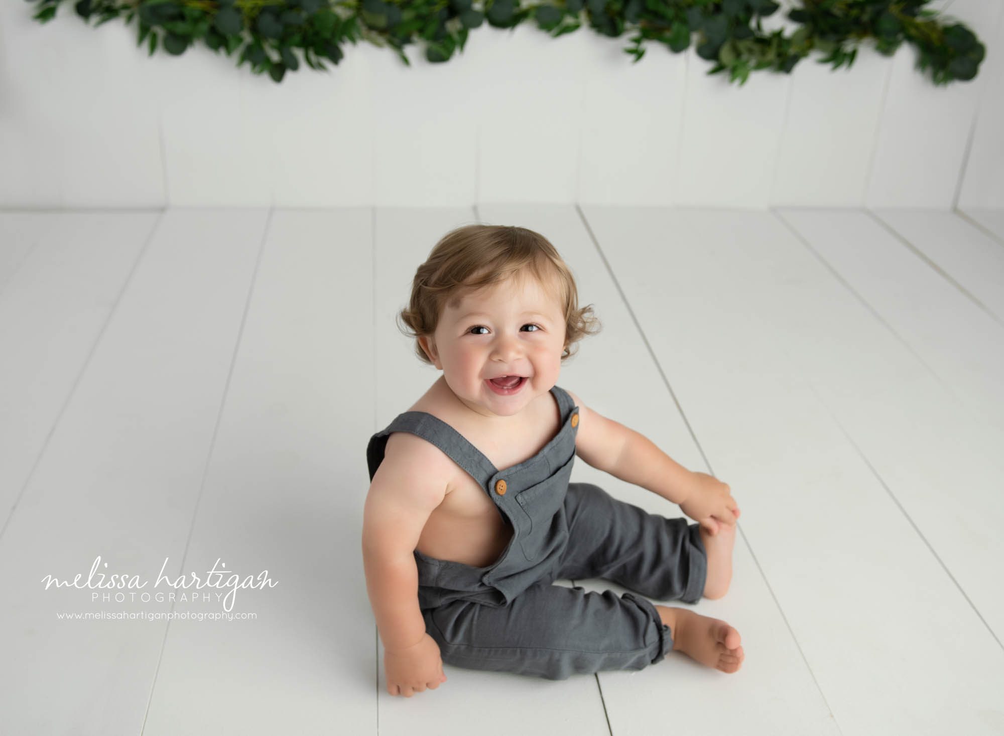 baby boy sitting on wooden floor boards in photography studio happy laughing