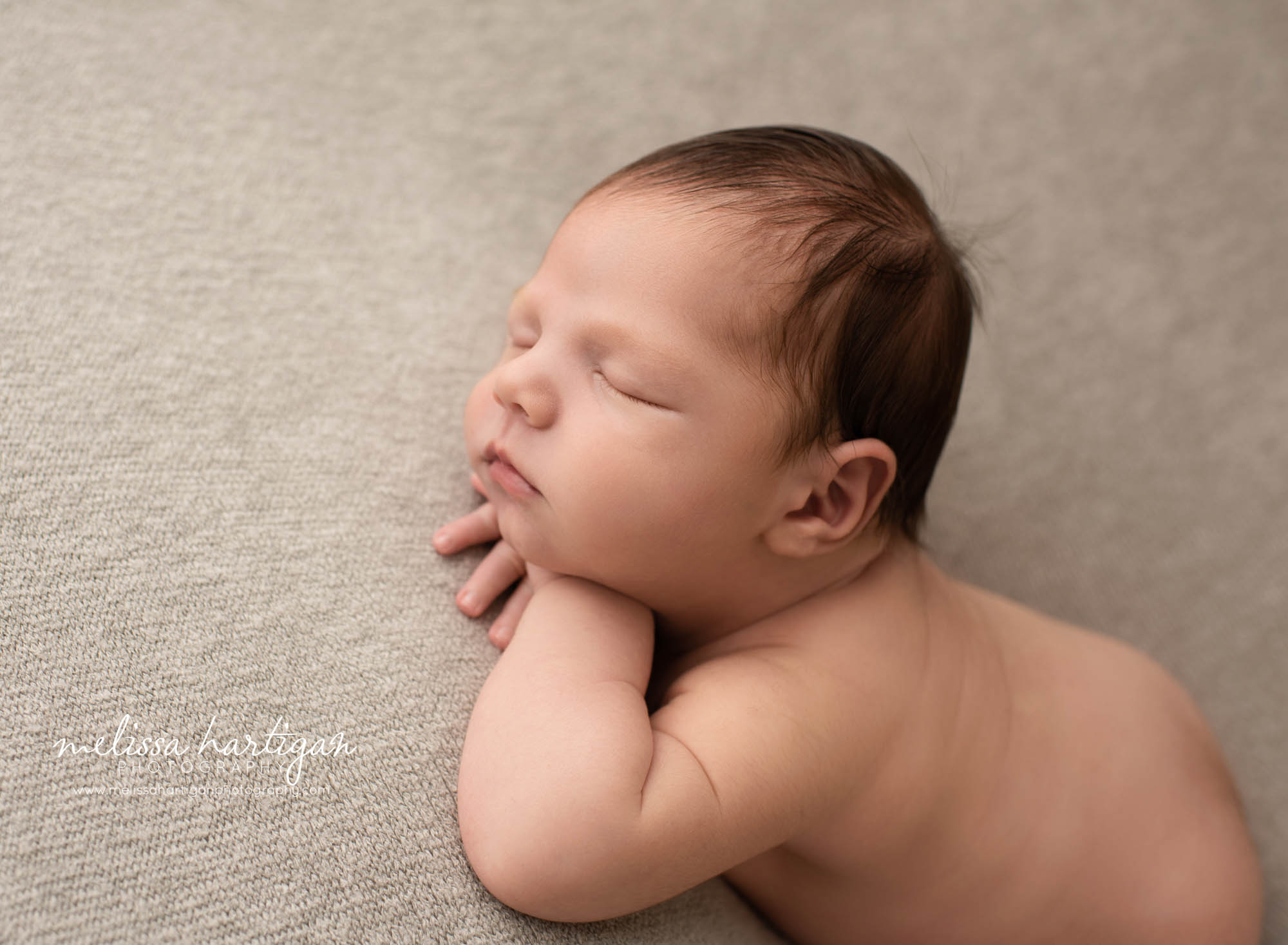 newborn baby boy posed on grey backdrop with hands under chin