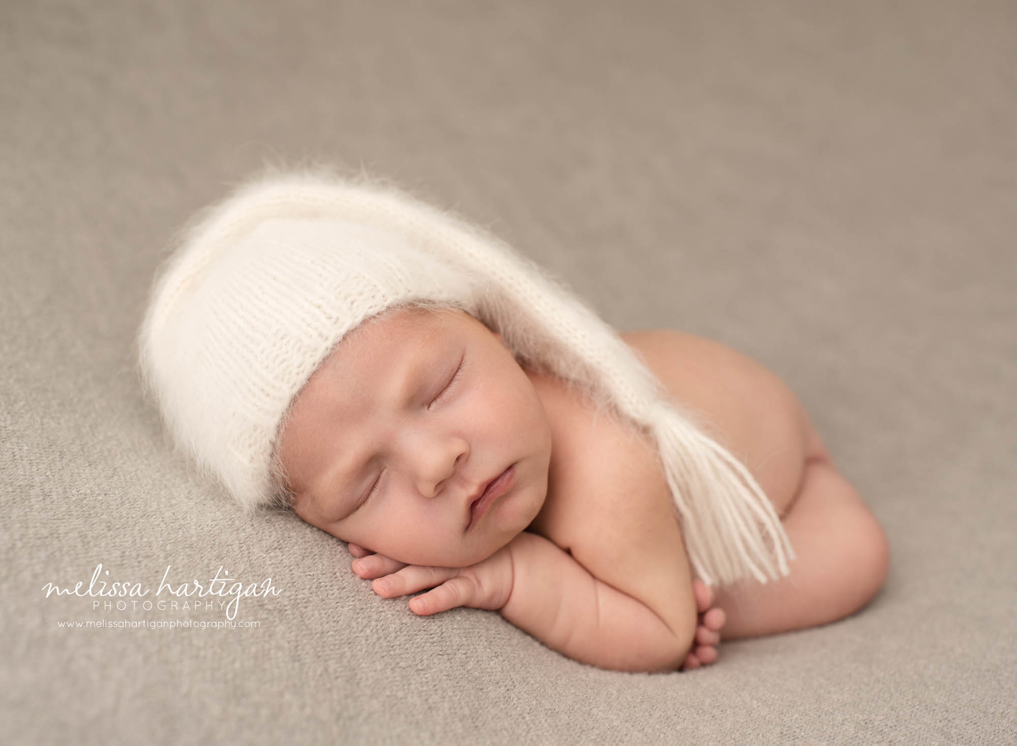 newborn baby boy posed modified taco pose wearing white knitted sleepy cap