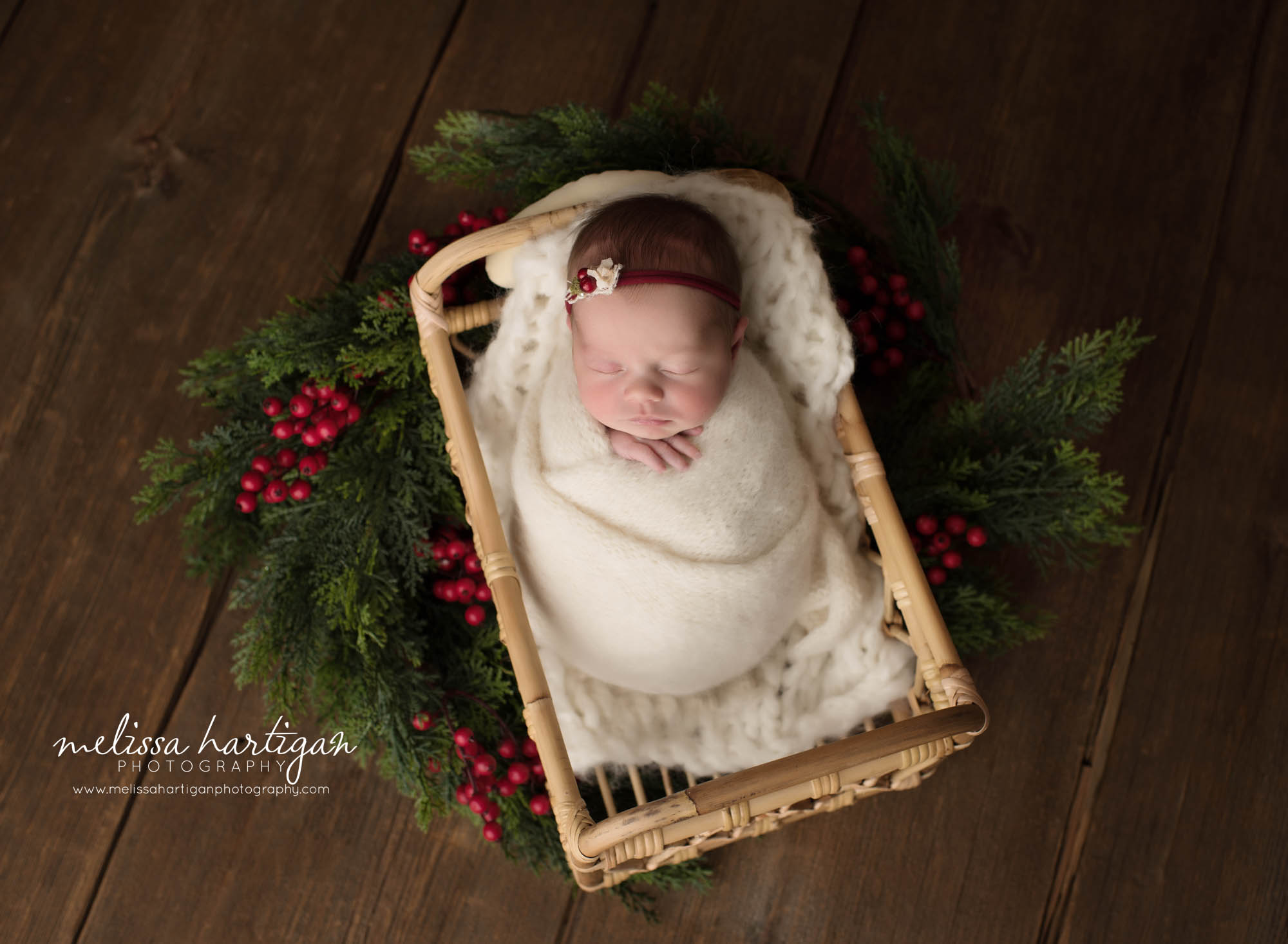newborn baby girl wrapped in white wrap posed in basket wearing red headband