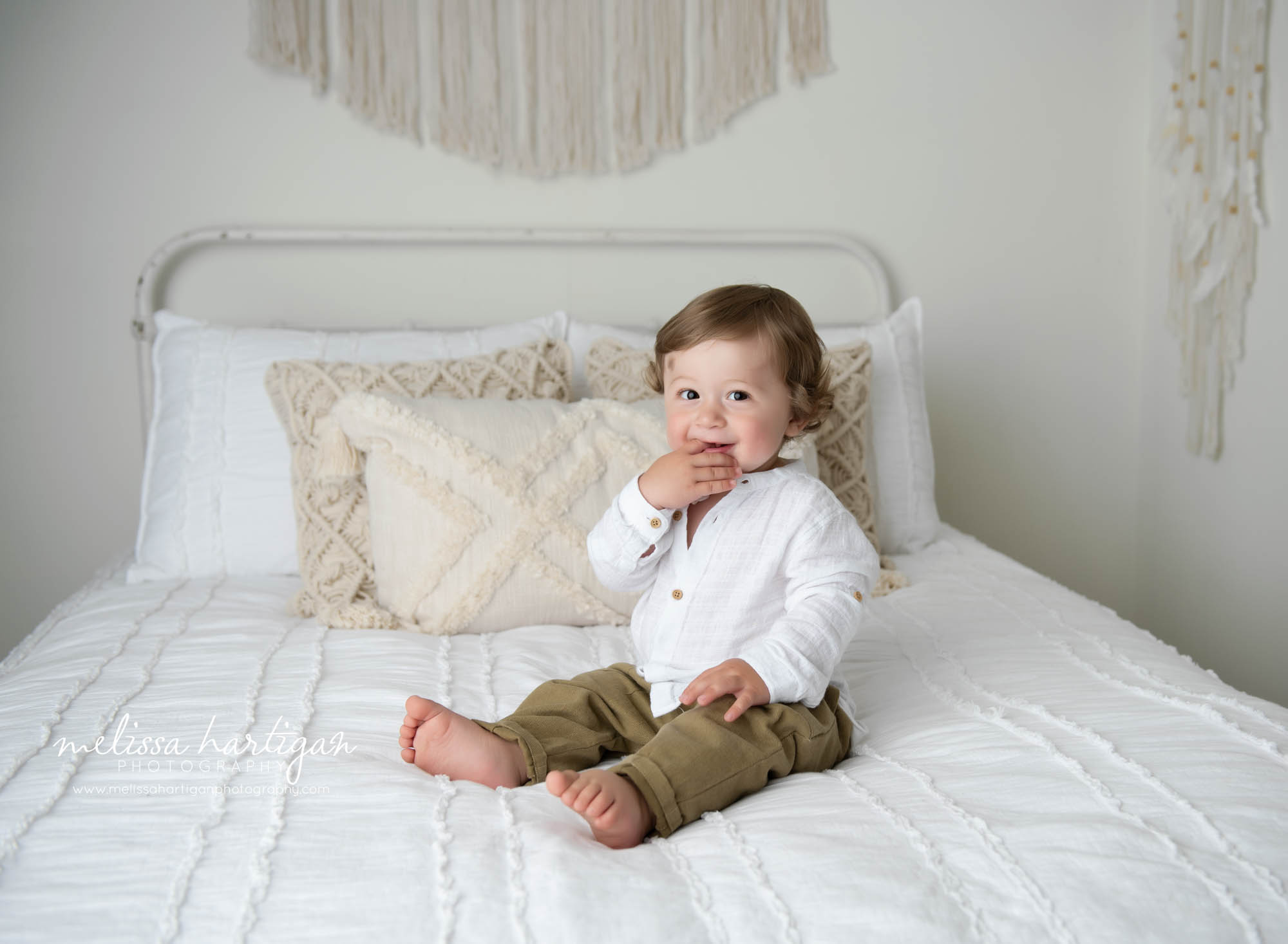 baby boy sitting on bed with fingers in mouth happy smiling saratoga county baby photographer