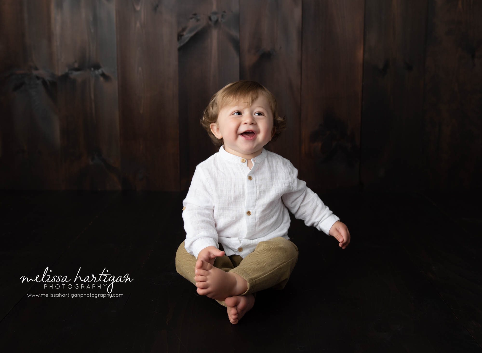 baby boy sitting on floor on wooden boards in baby photography studio