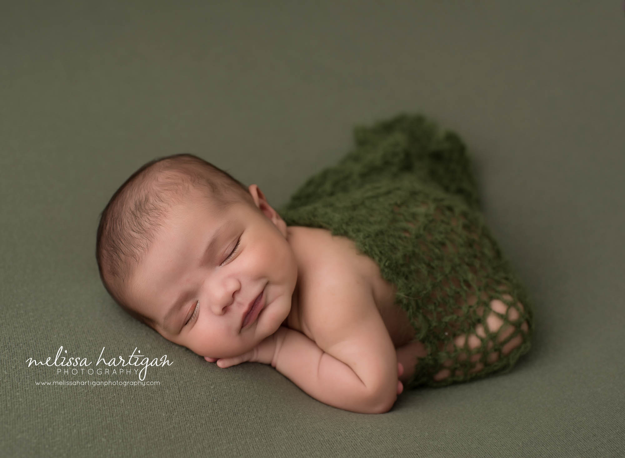 newborn baby boy posed on tummy with green knitted layer draped over