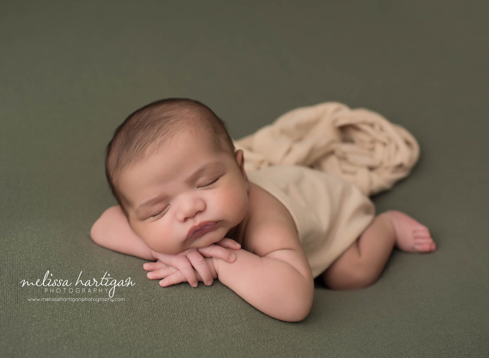 newborn baby boy posed on tummy with hands under chin with cream wrap draped over