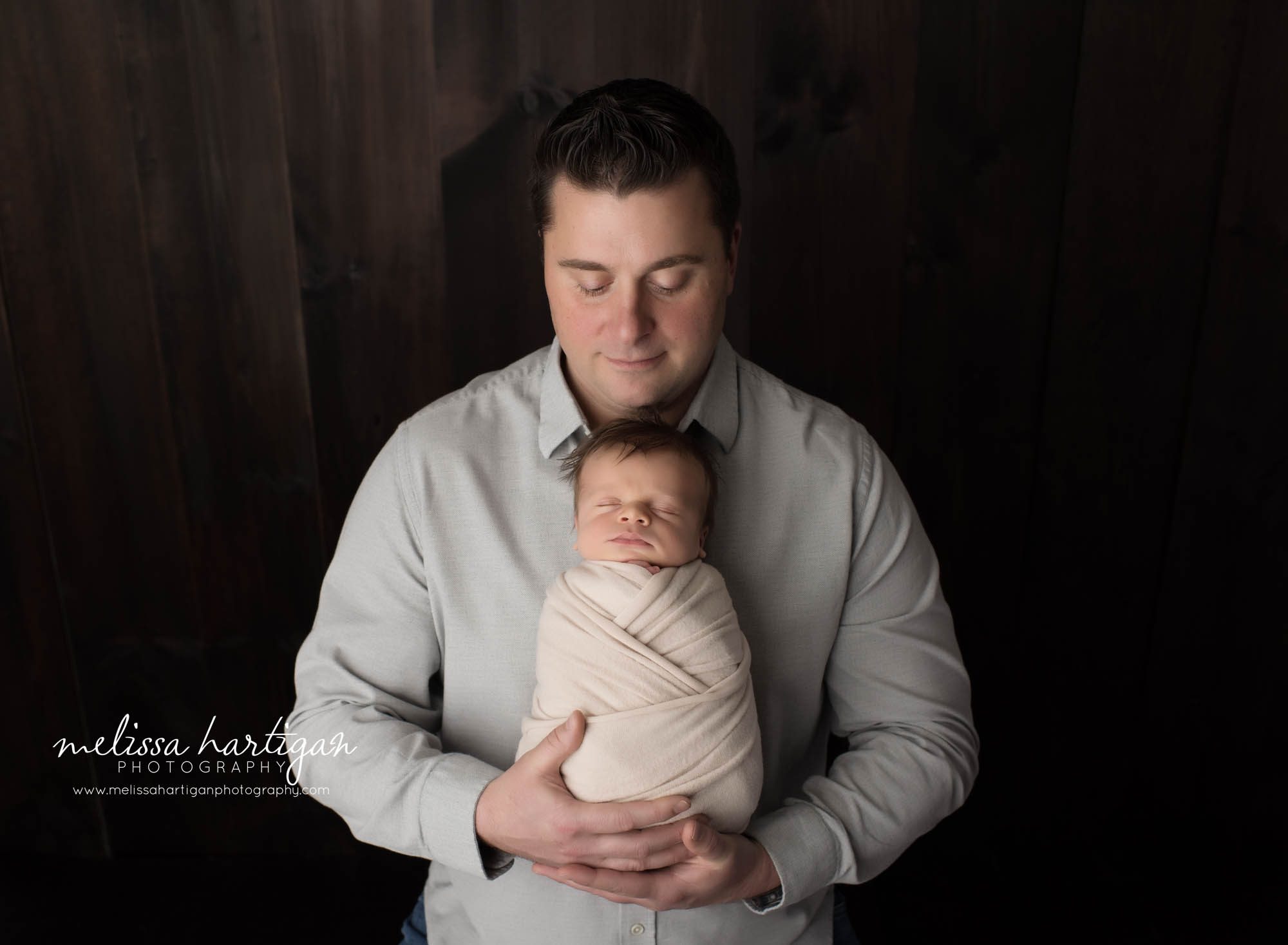 dad holding newborn son wrapped in cream wrap posed in front