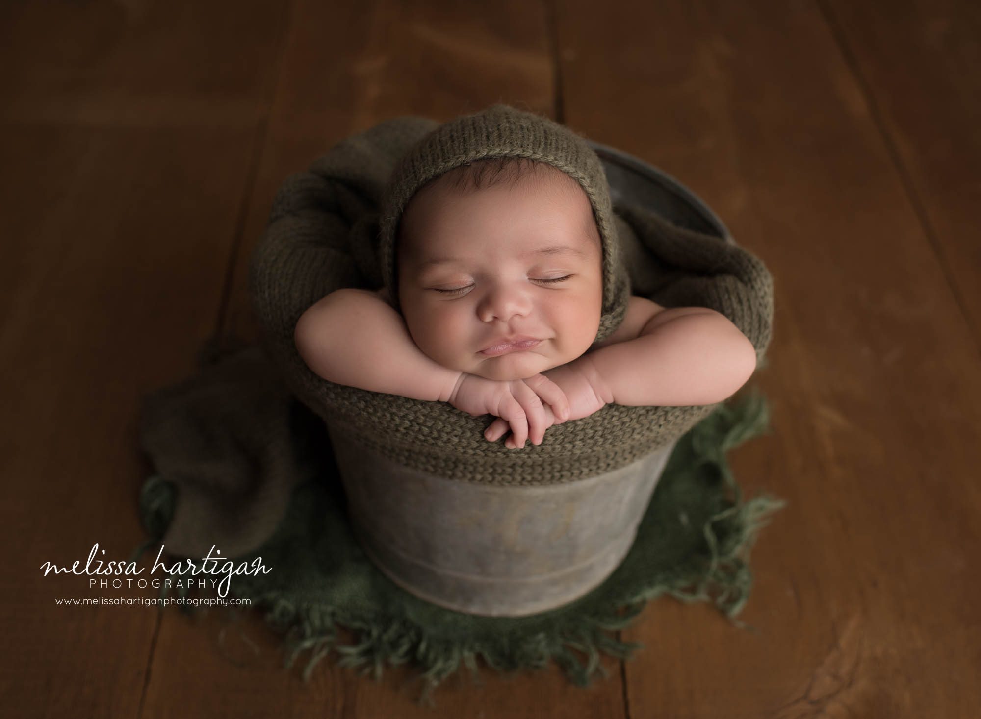 newborn baby boy posed in bucket with chin resting on hands smiling baby ct newborn photographer