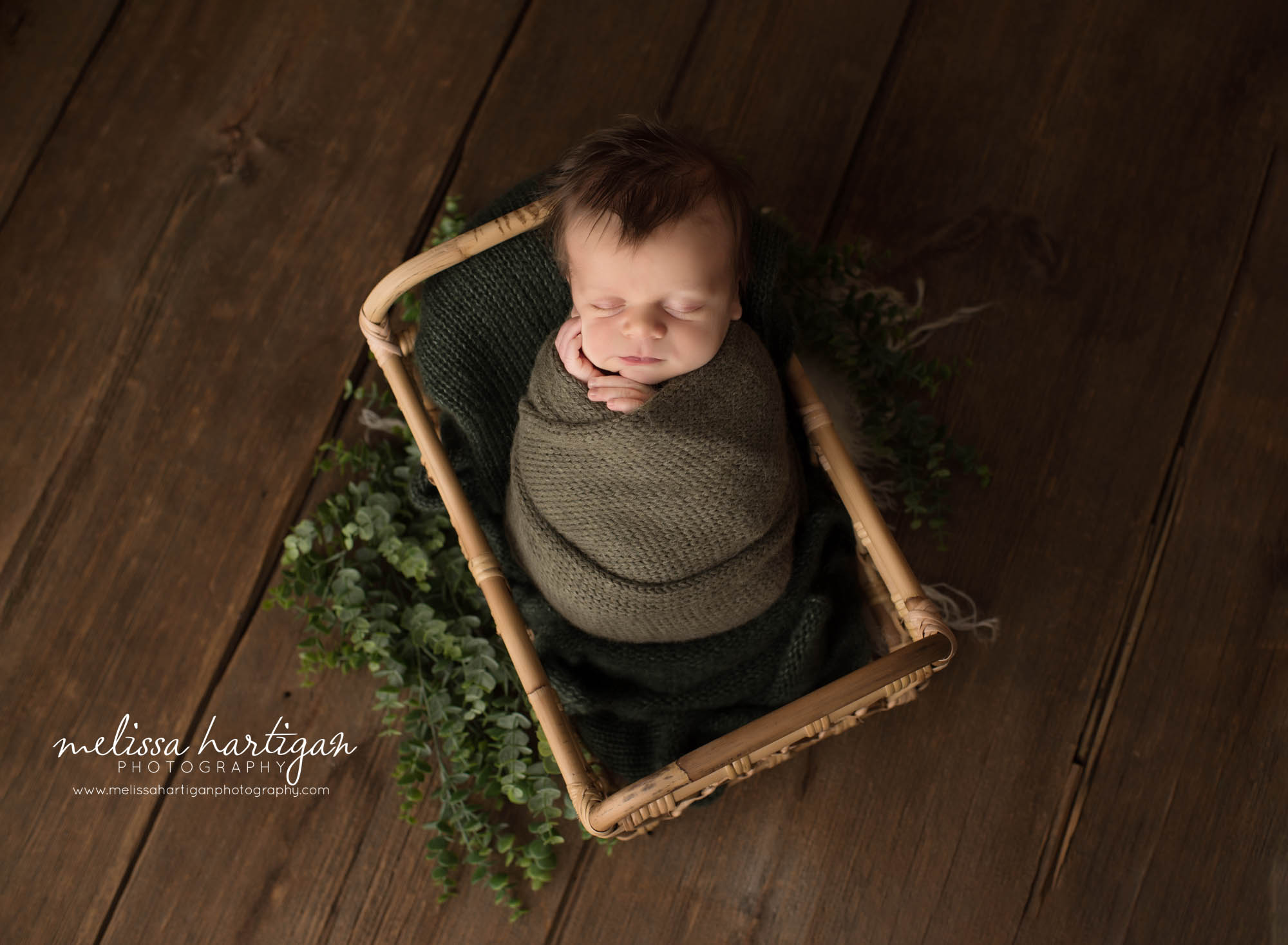 newborn baby boy posed in basket wrapped in green wrap
