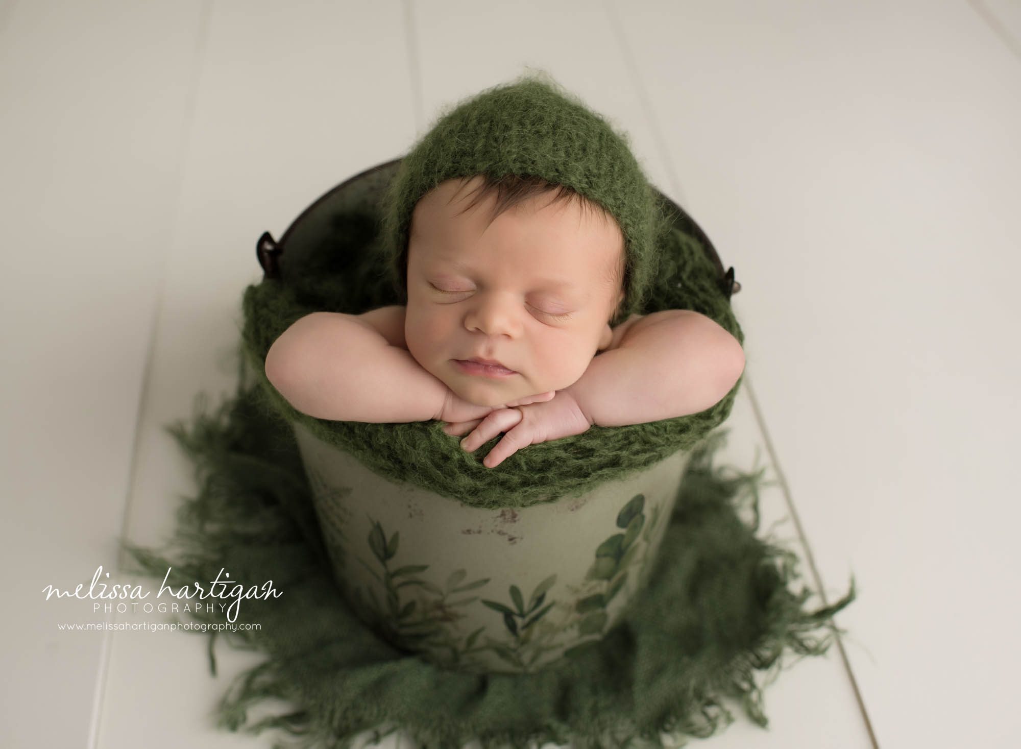newborn baby boy posed in bucket wearing knitted green bonnet newborn photography ct