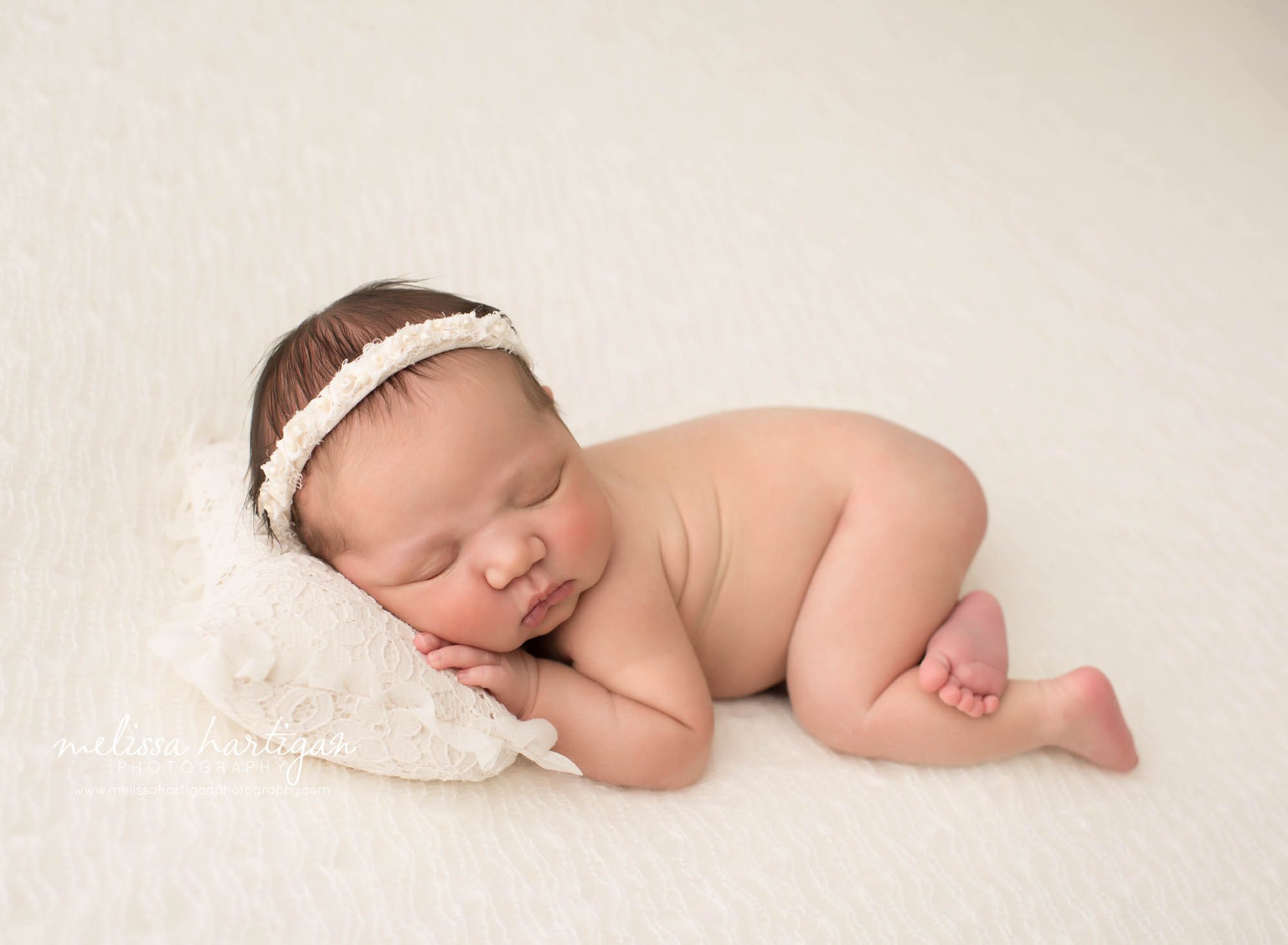 newborn baby girl posed on side with head on pillow wearing headband newborn photography south windsor ct