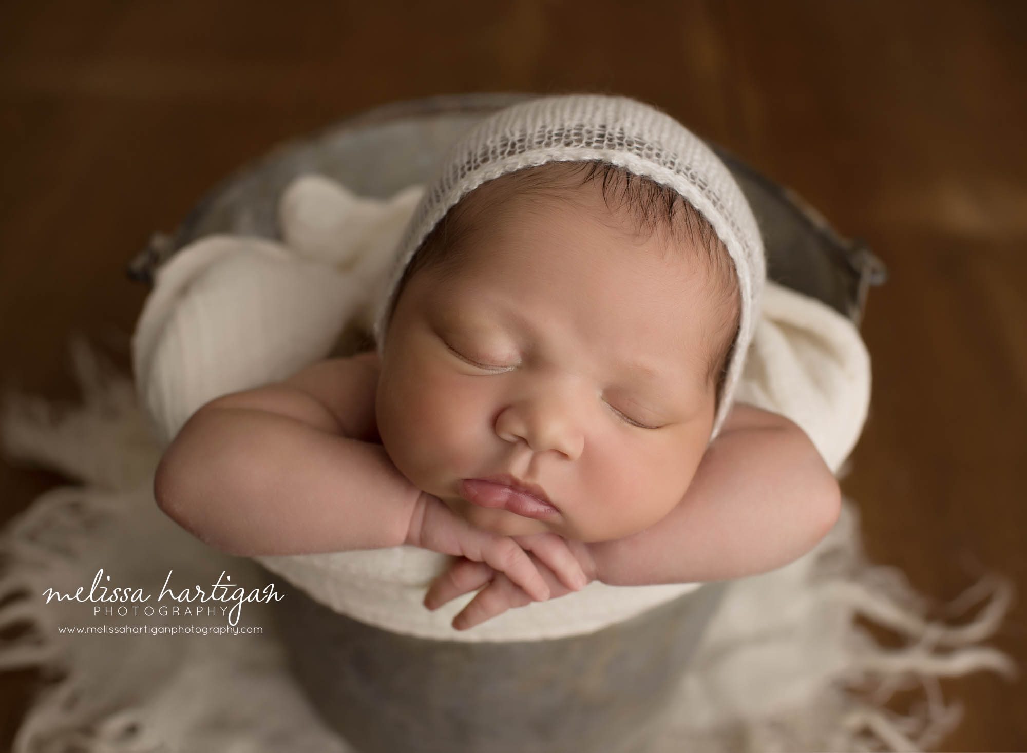 newborn baby girl posed in bucket wearing white knitted bonnet newborn photography CT