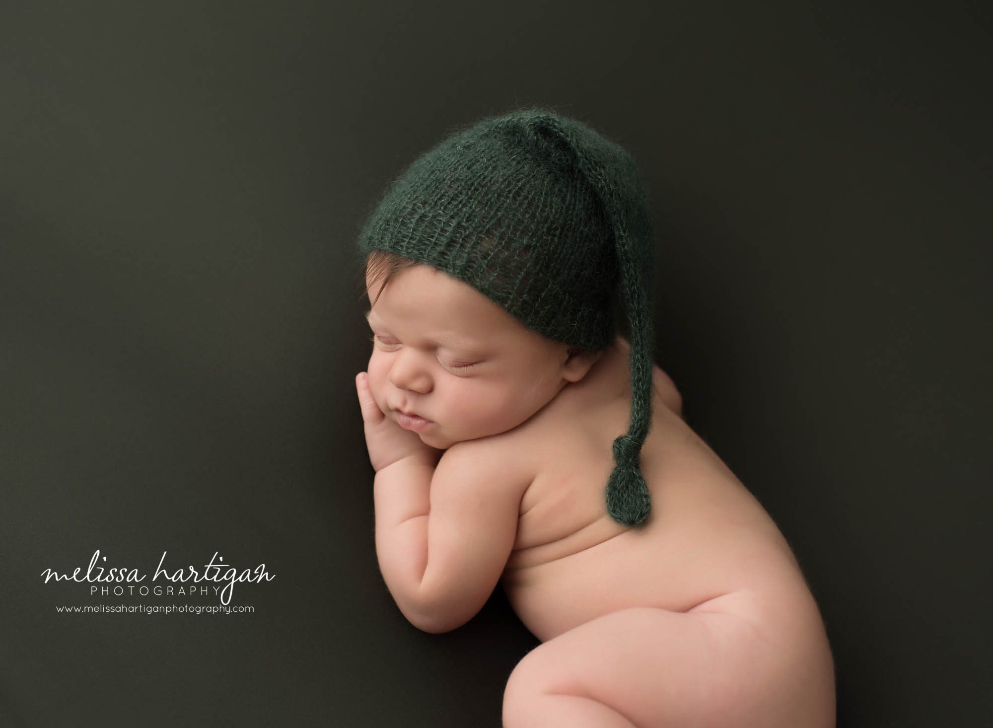 newborn baby boy posed on side tummy wearing knitted green sleepy cap