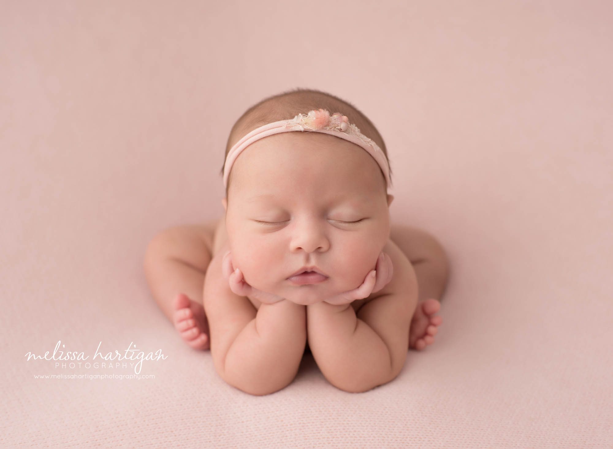 newborn baby girl posed froggy pose on pink backdrop