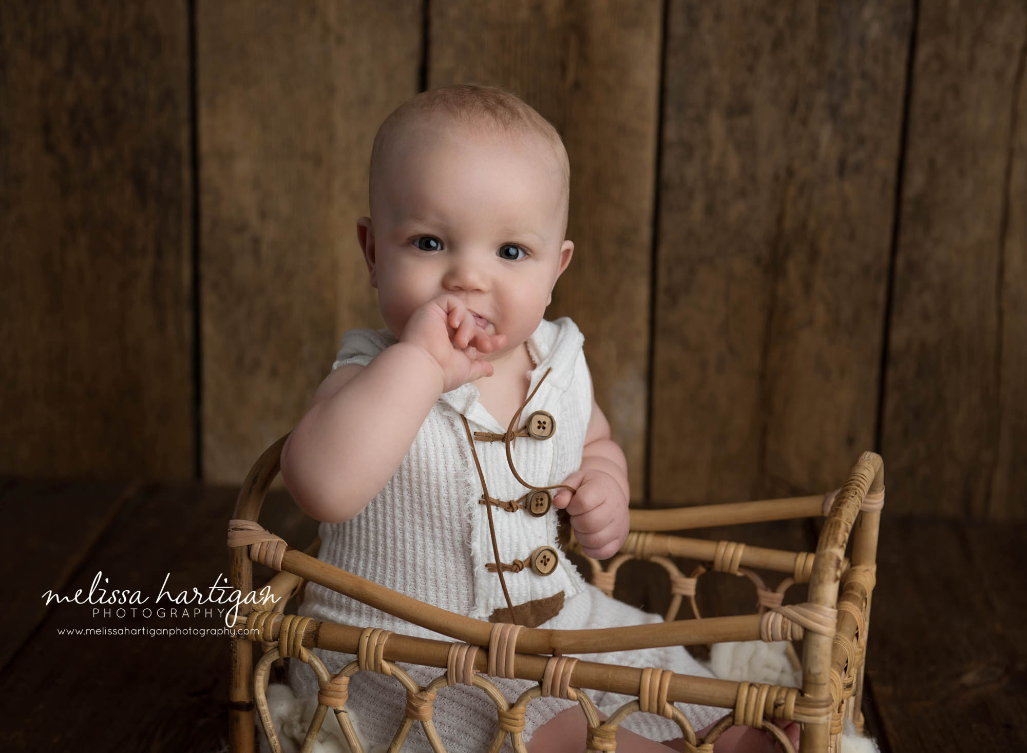 baby boy sitting in basket with fingers in mouth