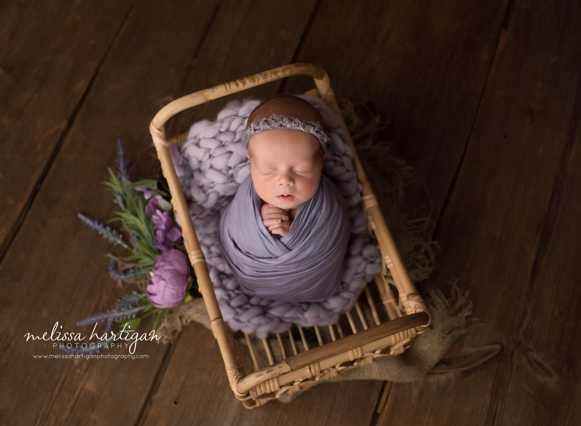 newborn baby girl posed in basket wrappe din purple wrap