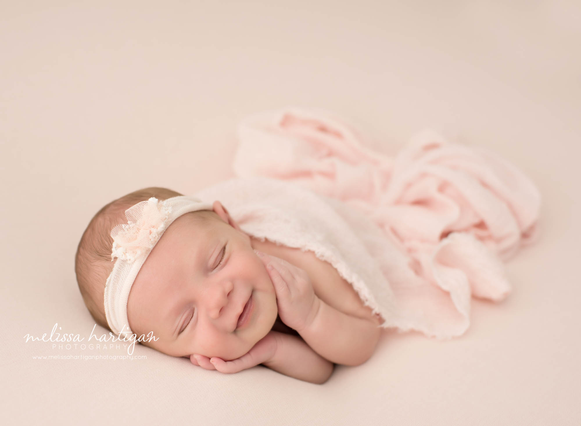 newborn baby girl posed on side smiling wearing cream and blush pink headband ct newborn photography connecticut baby photoshoot