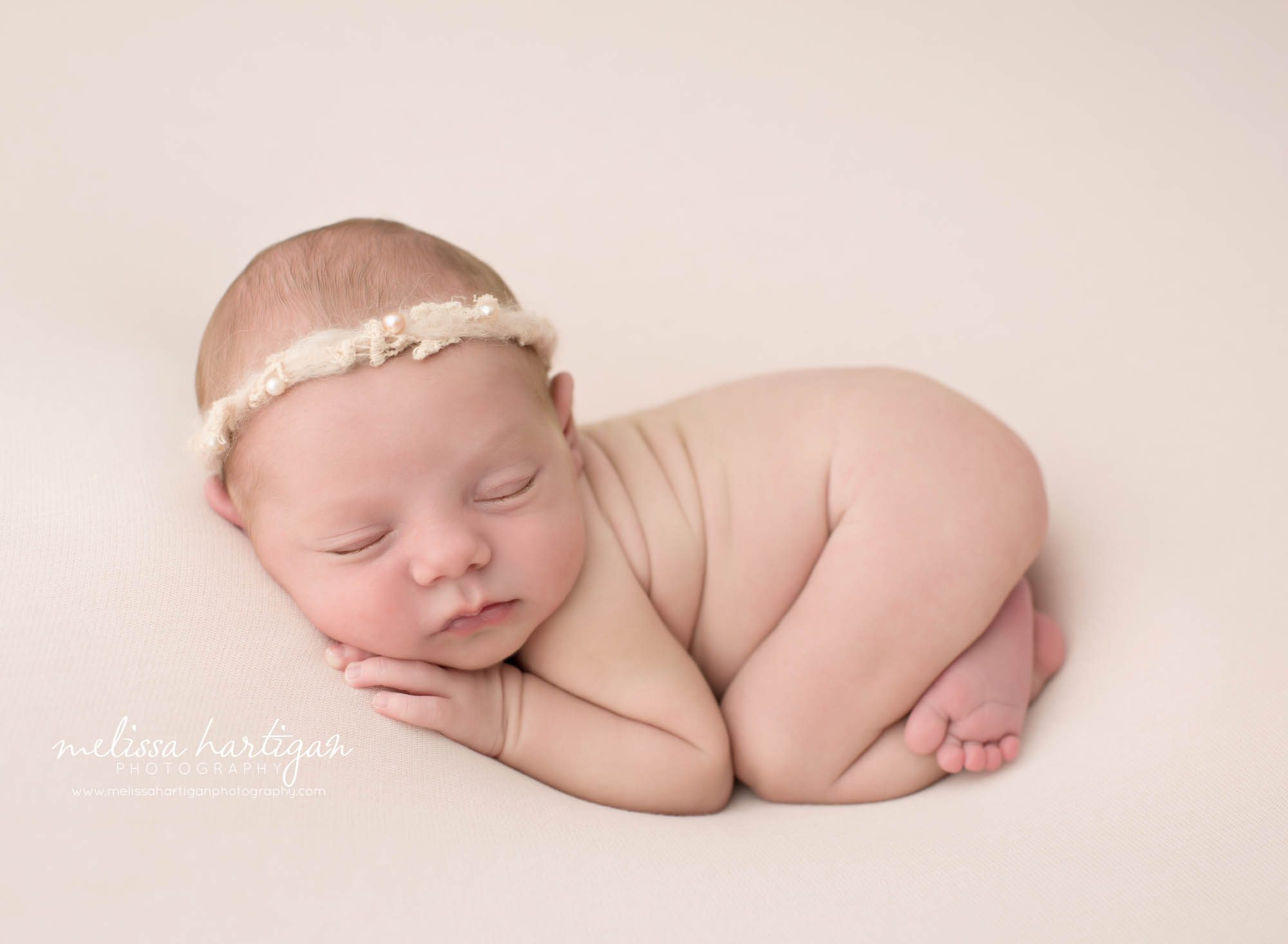 newborn baby girl posed on tummy on pink backdrop wearing headband