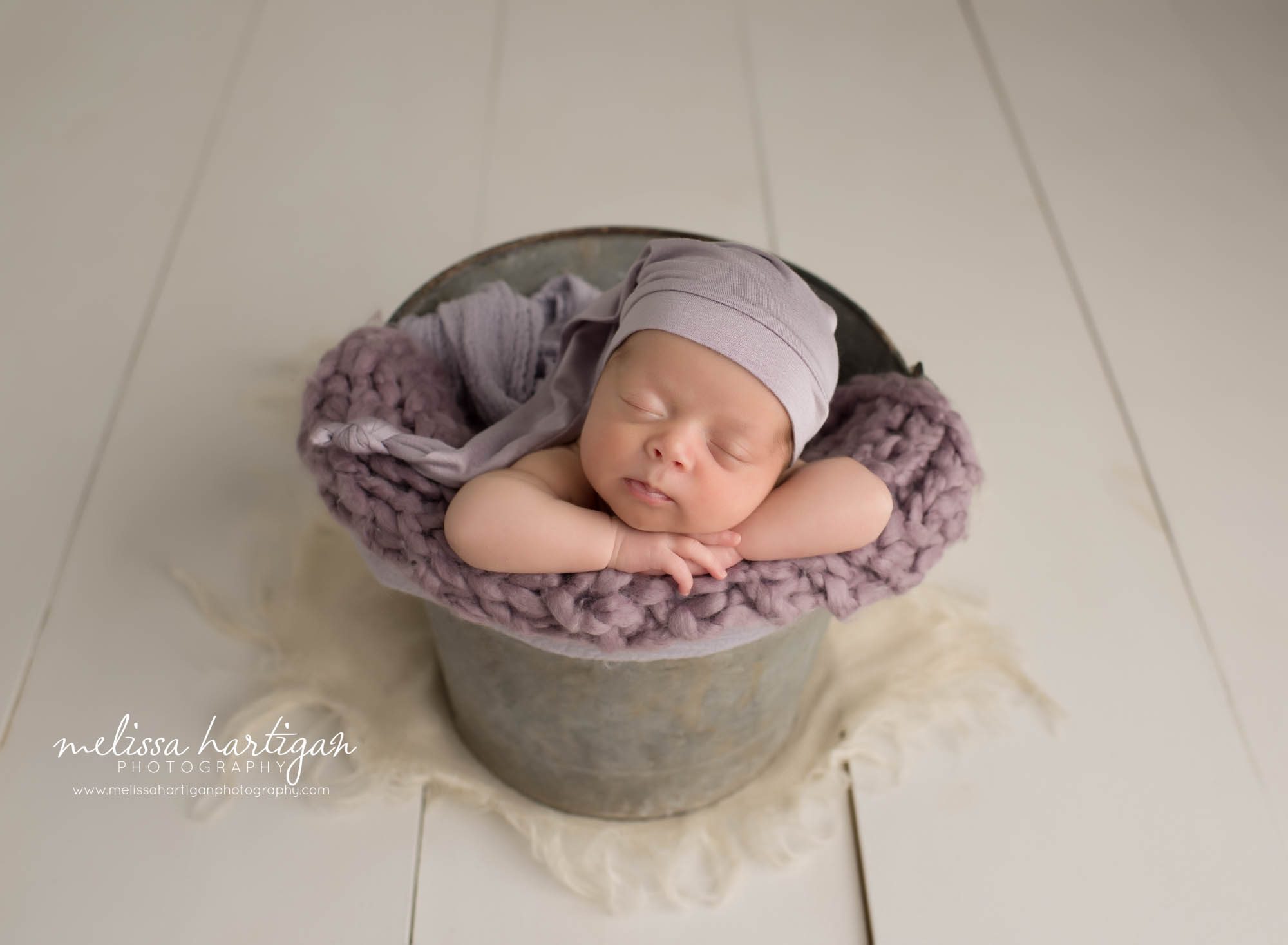 newborn baby girl posed in bucket wearing purple sleepy cap CT newborn photography