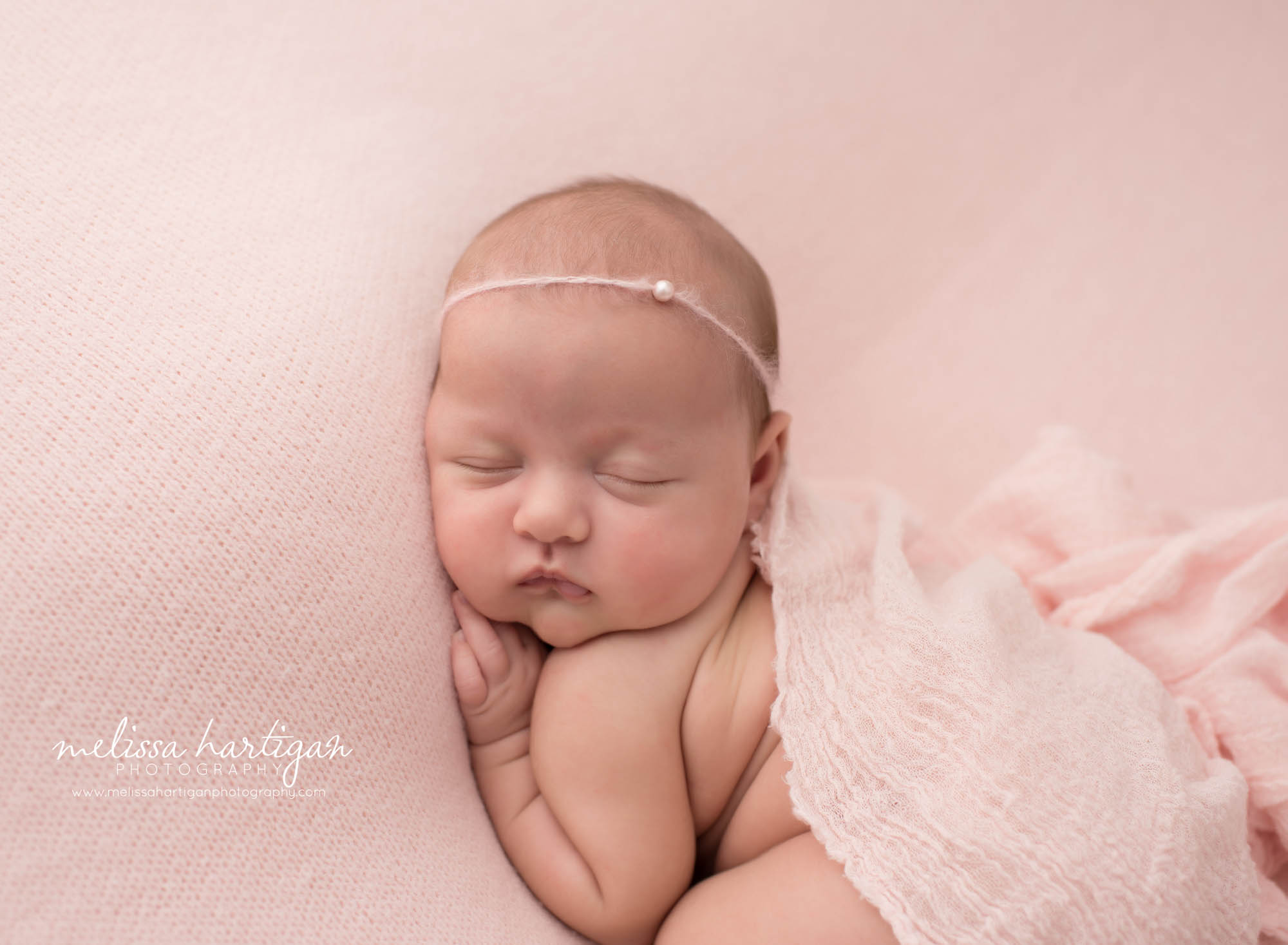 newborn baby girl posed on tummy wearing pink bead headband and pink layer draped over her backside