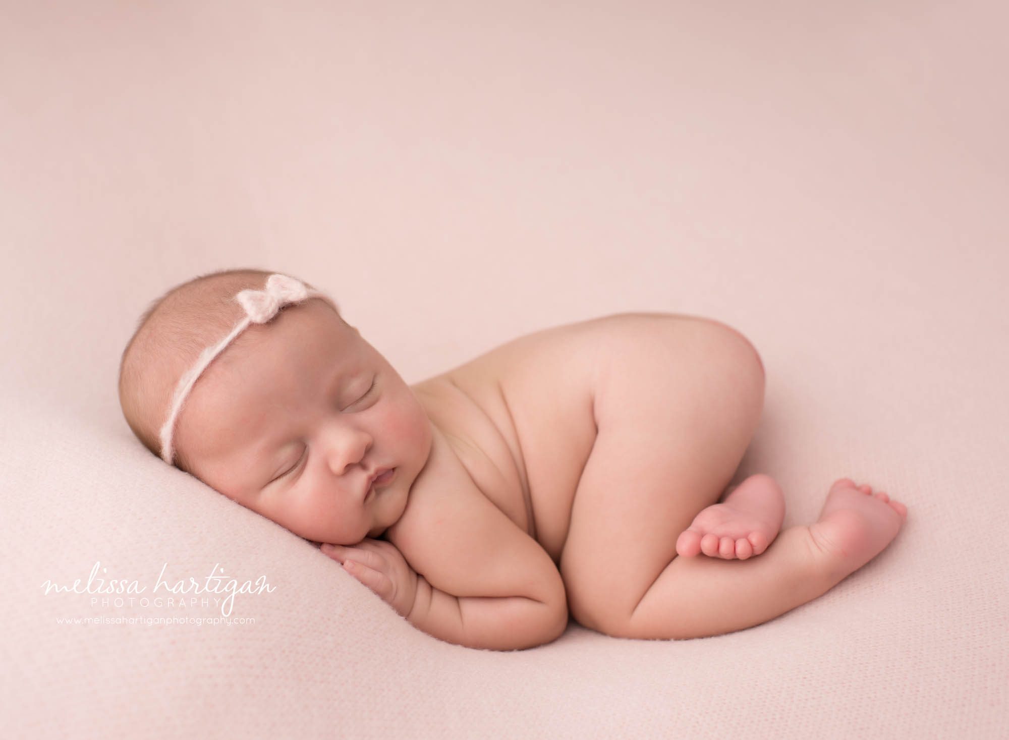 newborn baby girl posed on tummy on pink backdrop wearing pink bow headband baby photography new london county