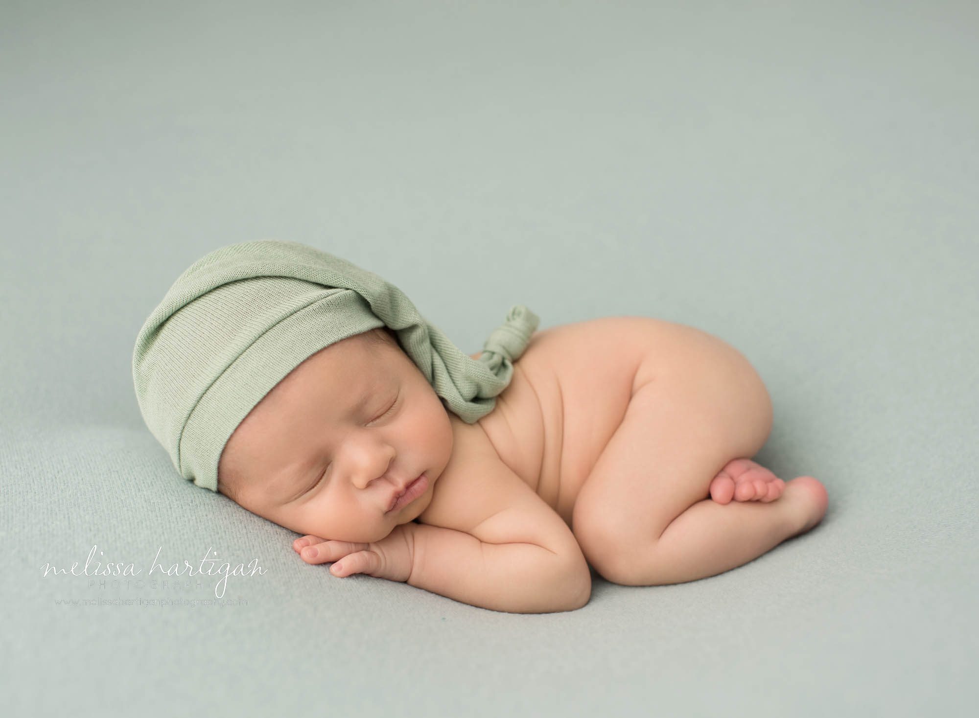 newborn baby boy posed on tummy wearing green sleepy cap newborn photography tolland county ct