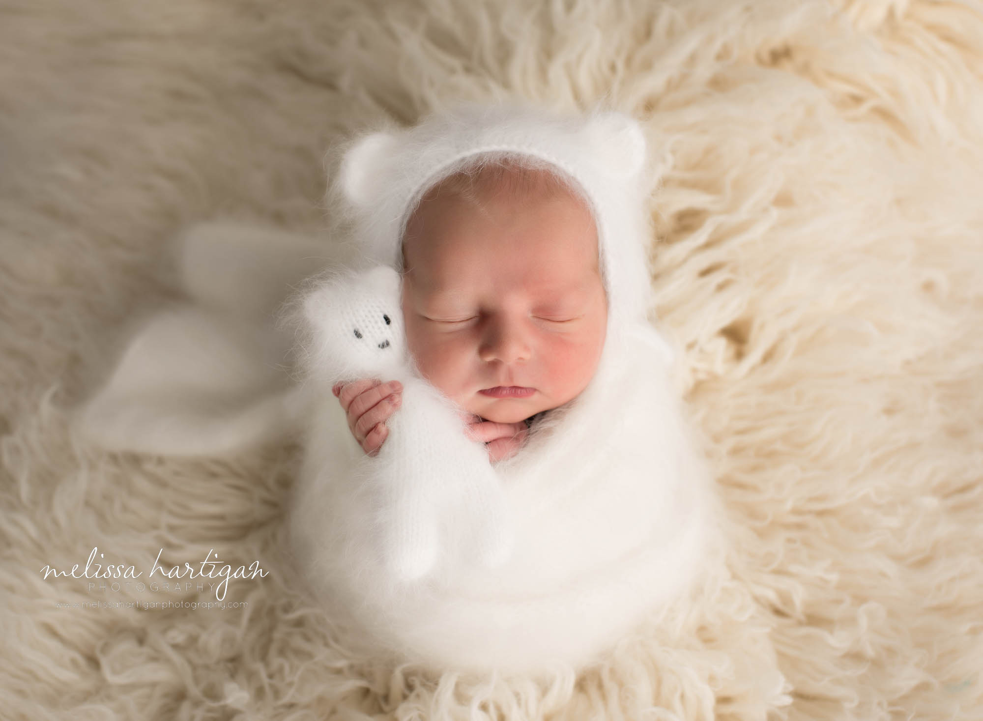 newborn abby boy posed on cream flokati wearing knitted bear bonnet holding matching teddy