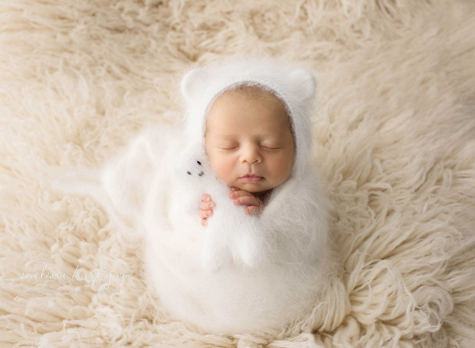 newborn baby boy wrapped in cream white knitted layer wrap wearing matching bear bonnet holding teddy